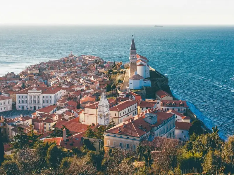 Panoramic view over Piran on Slovenia’s Adriatic coast, with terracotta rooftops and the hilltop church overlooking the blue Mediterranean sea. A peaceful coastal town scene that suits an article on the safest places to visit in Europe, highlighting Slovenia’s reputation as a calm, easy-to-navigate destination with a relaxed pace, walkable old towns, and a welcoming feel for mature travellers.