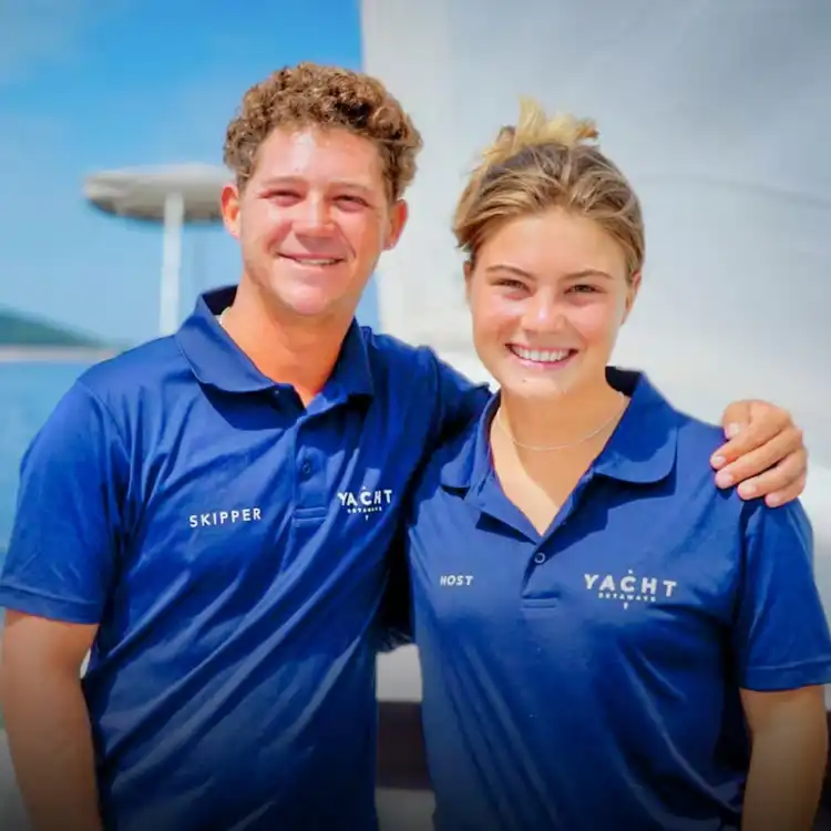 Yacht Getaways skipper and host in branded uniforms, smiling together on board — the expert crew guiding every Greece and Croatia sailing holiday.