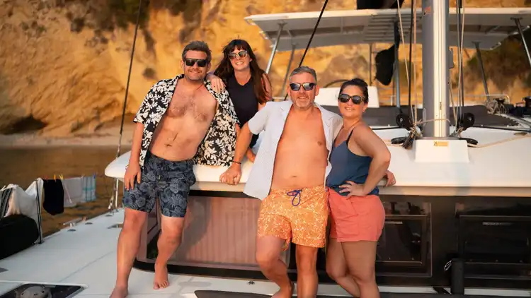 Two women stand on the front of a catamaran in Greece