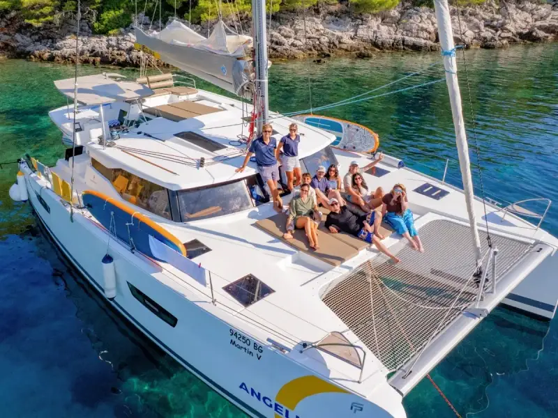 A small group of guests relaxing together on the deck of a catamaran in clear Mediterranean water, showing the social and restorative side of blue health travel. This image reflects the relaxed atmosphere of a luxury yacht holiday in Greece or Croatia, where time at sea, fresh air, swimming and shared moments on board create a more meaningful wellness escape.