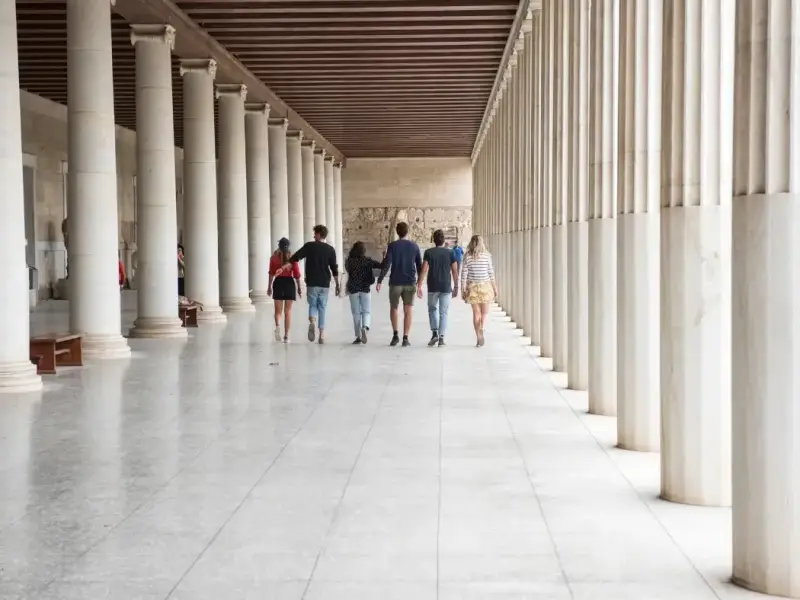 Travellers walking through the colonnaded Stoa of Attalos in the Ancient Agora of Athens, Greece. This image suits an Athens travel guide focused on historic sites, ancient landmarks, and the best places to visit in Athens beyond the Acropolis.