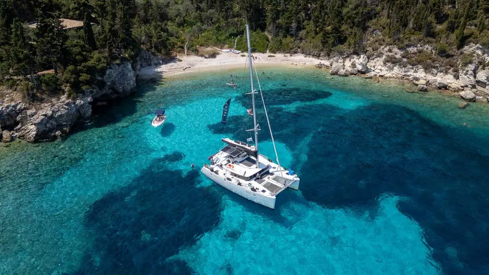 Drone image of a luxury catamaran anchored in a bright blue bay near Paxos island in Greece while on a luxury catamaran cruise with Yacht Getaways.