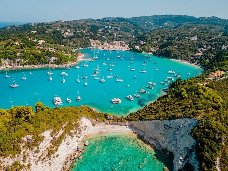 Aerial photo of Lakka on Paxos Island in Greece with a bay filled of anchored yachts on beautiful blue water.