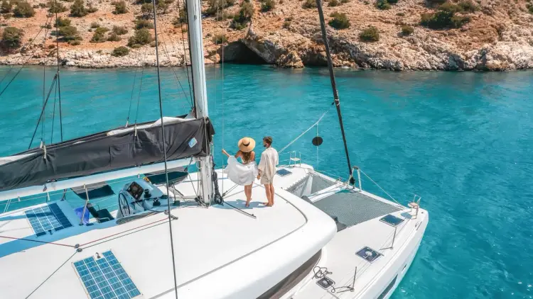 Couple standing on the deck of a luxury catamaran anchored in turquoise water during a Yacht Getaways sailing holiday in Greece.
