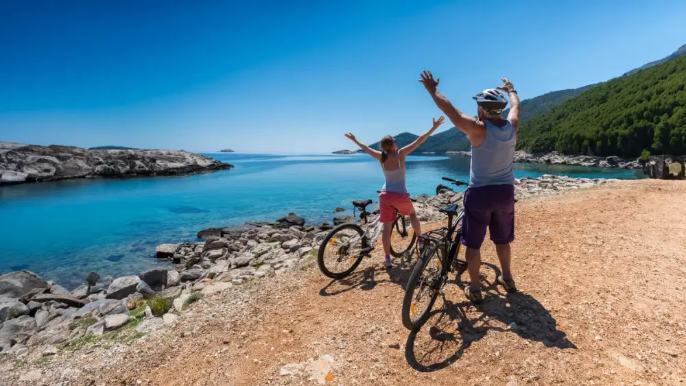 A couple holds their hands up while resting by the turquoise lakes of Mljet National Park during a cycling cruise in the Croatian islands.