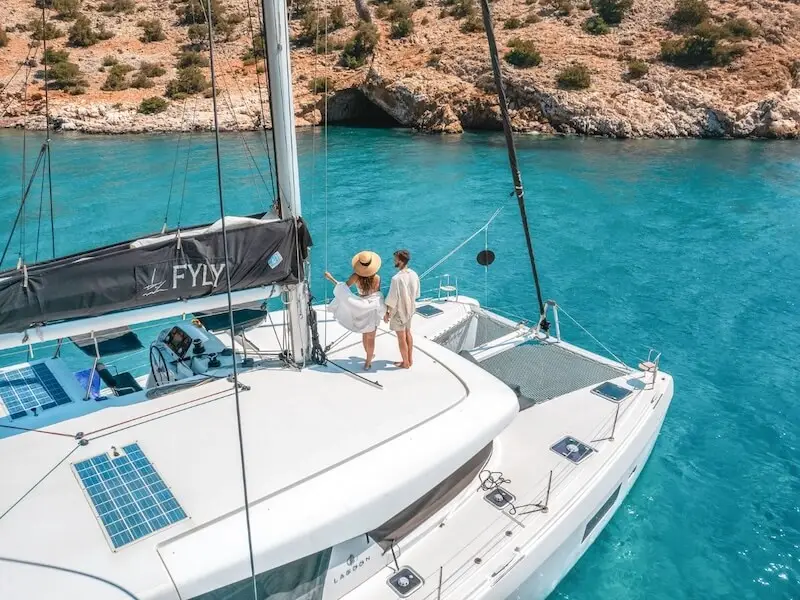 A couple enjoy paradise on a luxury catamaran cruise in Greece anchored in a secluded bay with a sea cave.