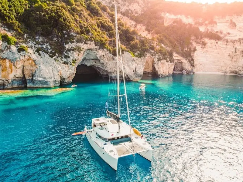 Aerial photo of a luxury catamaran anchored in a beautiful blue bay with a sea cave nearby on Paxos island. Visited while on a luxury catamaran vacation in Greece. 