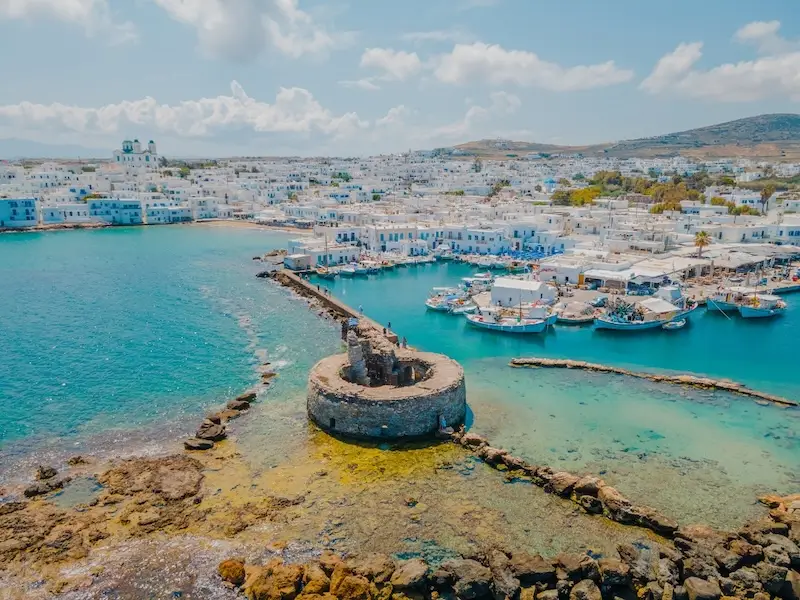 A beautiful drone photo of Naoussa on Paros Island in Greece, showing white-washed villas and blue waters, one of the best Greek islands to visit for summer.
