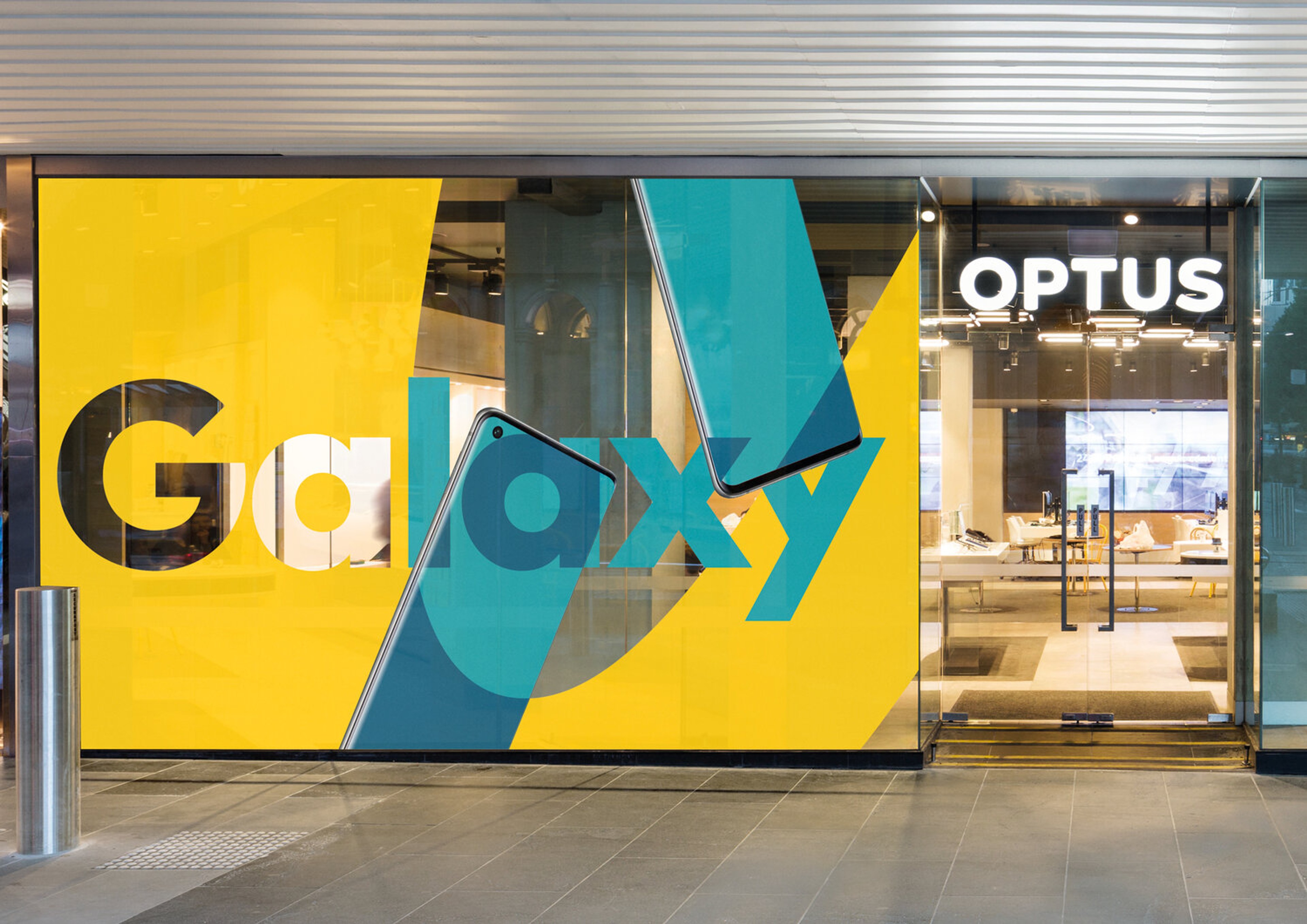 Yellow shopfront window graphic for Galaxy beside the illuminated Optus store sign