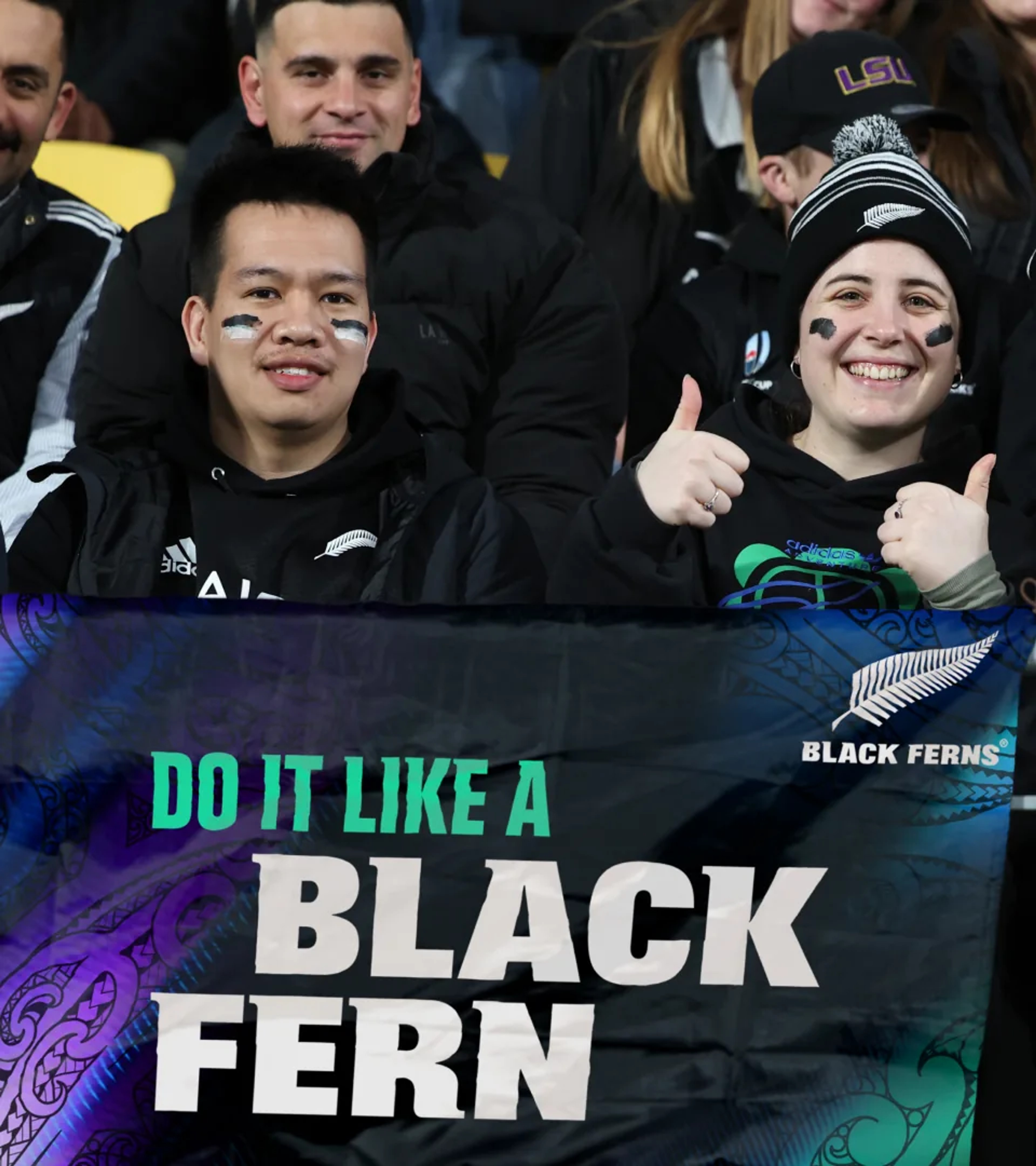 Fans in the stands holding a "Do it like a Black Fern" banner with Māori pattern