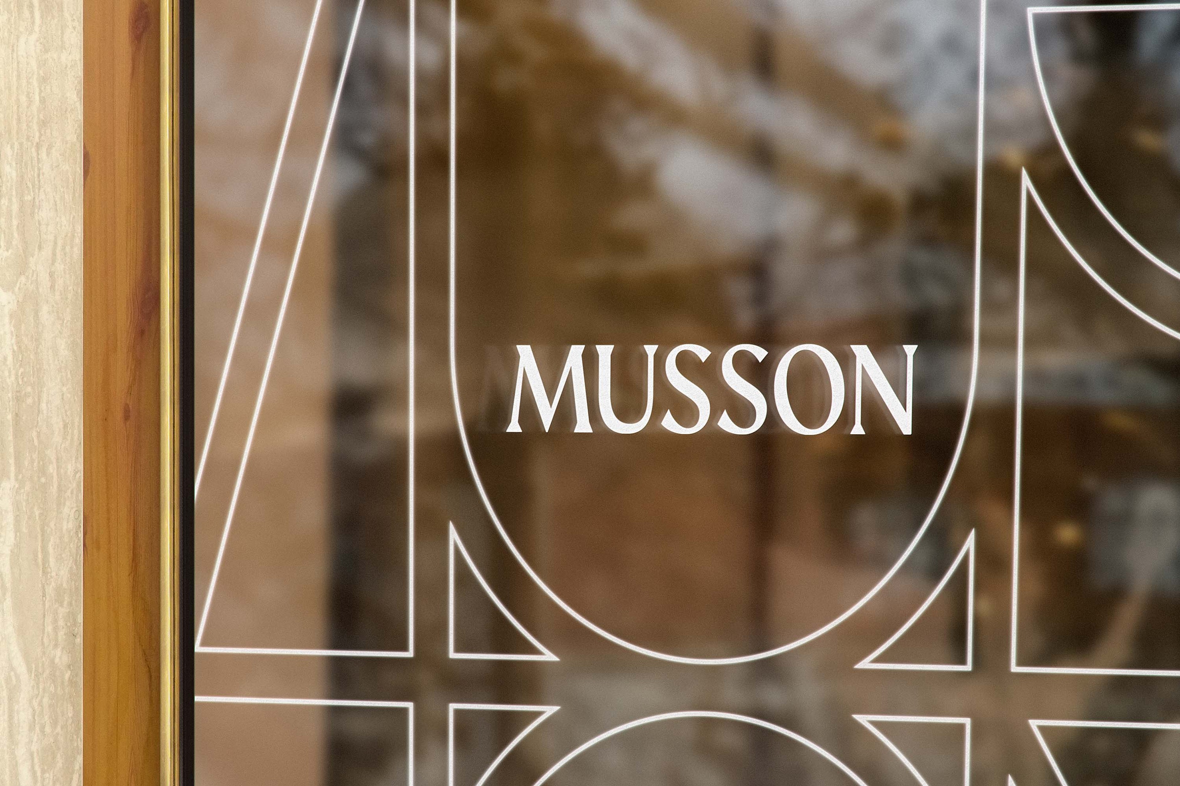 Etched glass shopfront window carrying white outline monogram lines and the Musson wordmark