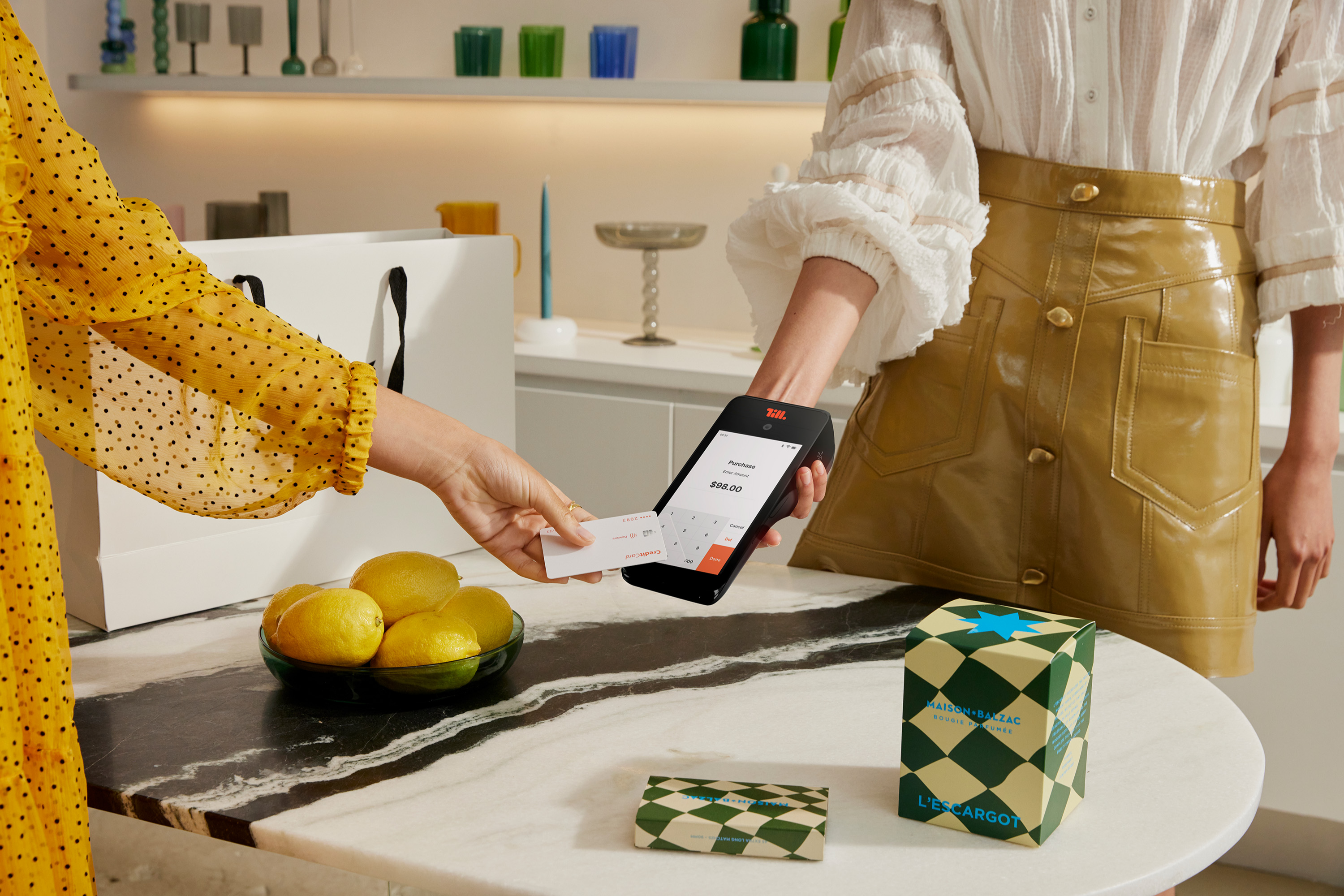 Customer tapping a card on a payment terminal at a marble counter with lemons and packaging