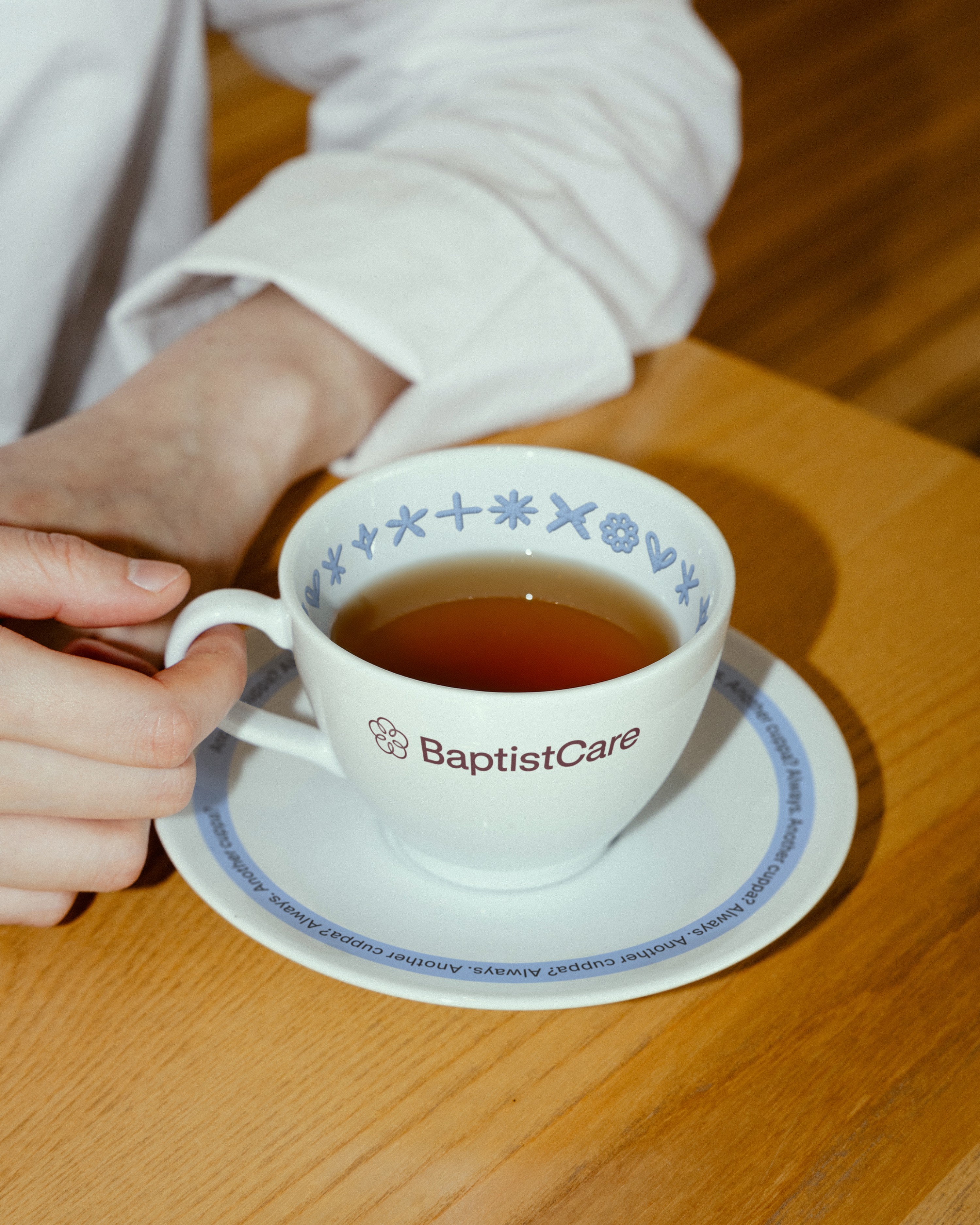 Hand cradling a branded teacup and saucer patterned with the small stitched icon set