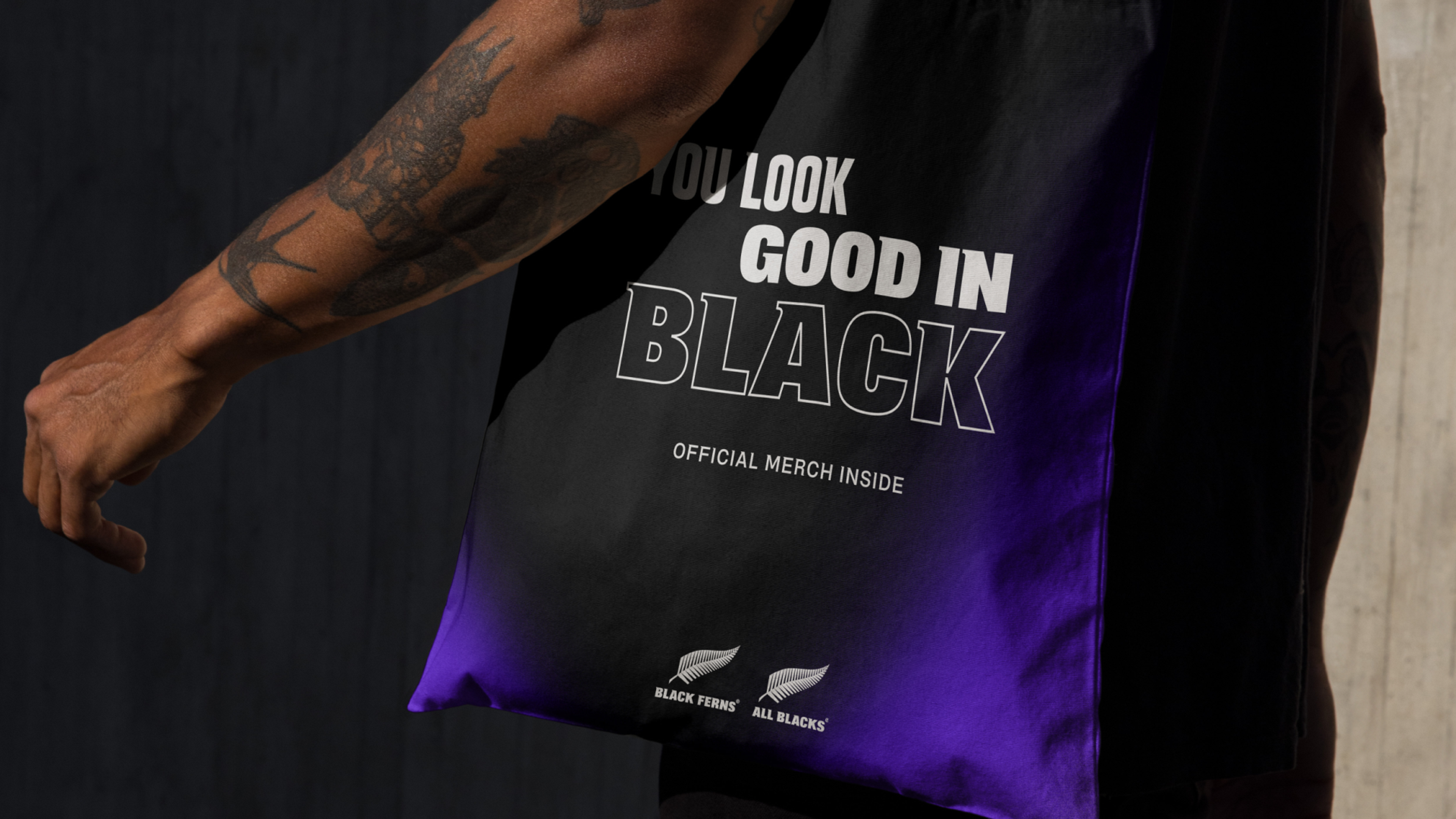Tote bag carried under an arm, fading black to purple, reading "You look good in black"