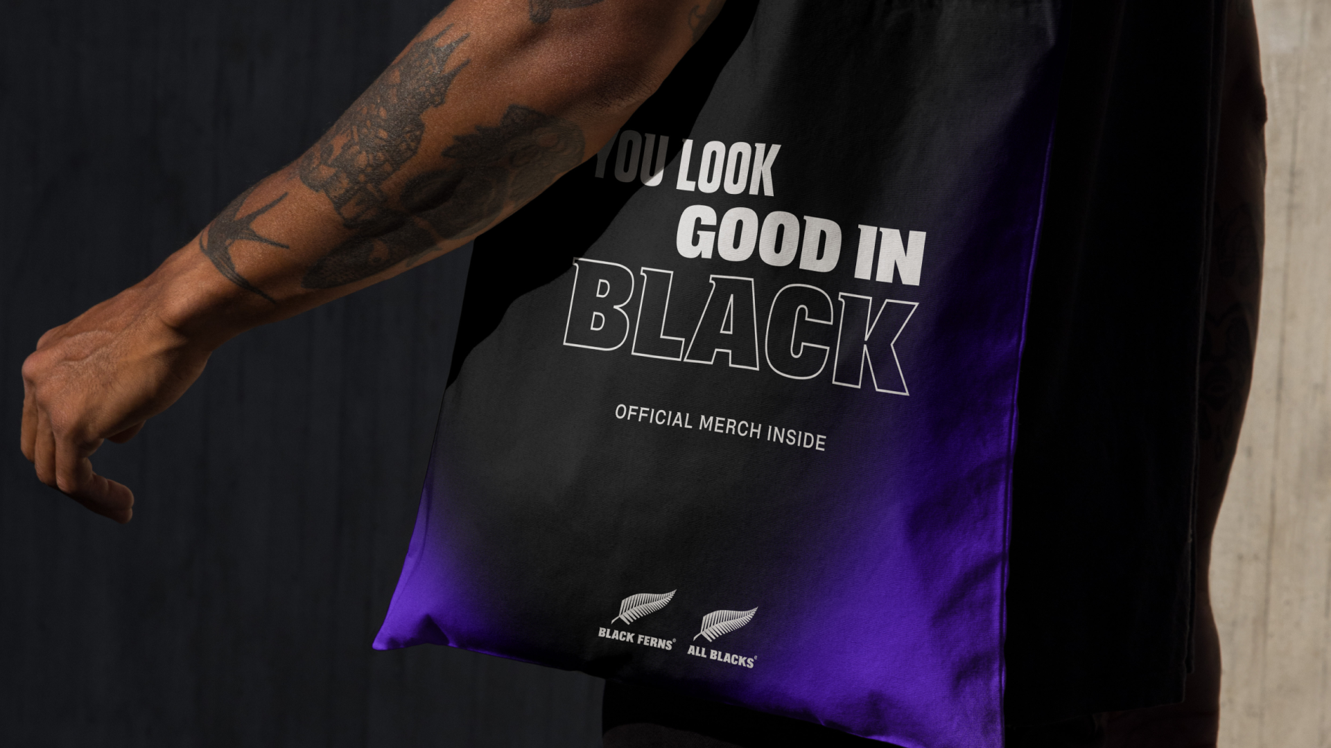 Tote bag carried under an arm, fading black to purple, reading "You look good in black"
