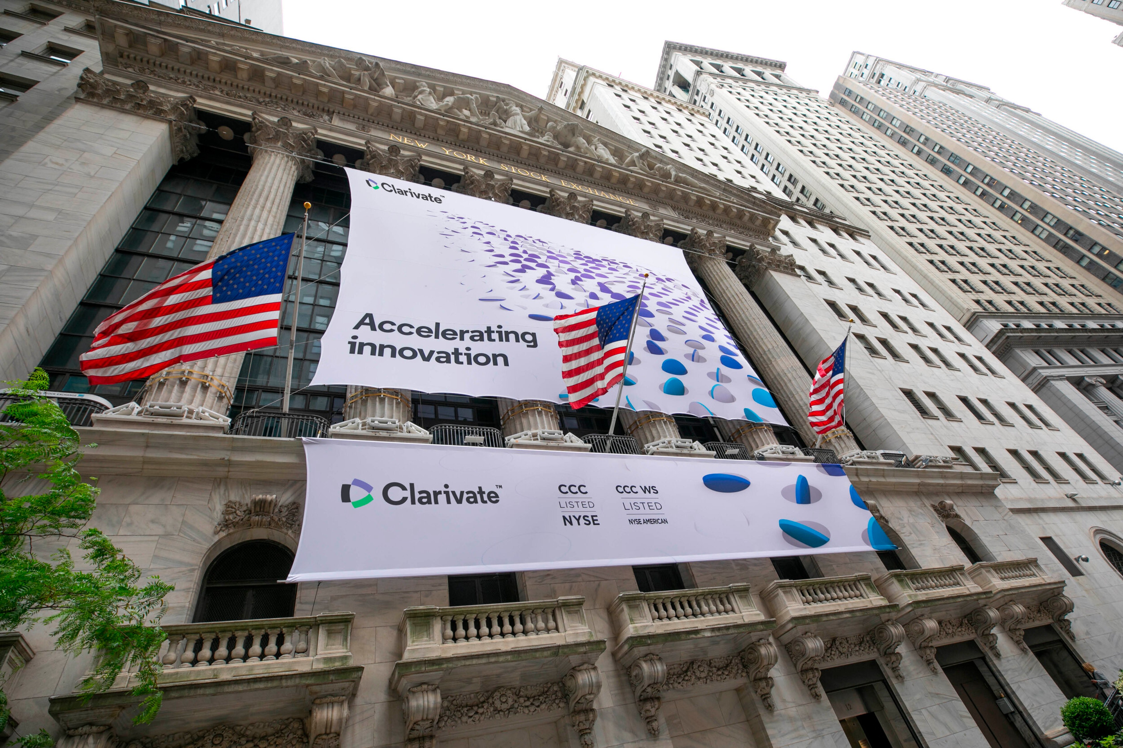Clarivate listing banners on the New York Stock Exchange facade, reading Accelerating innovation