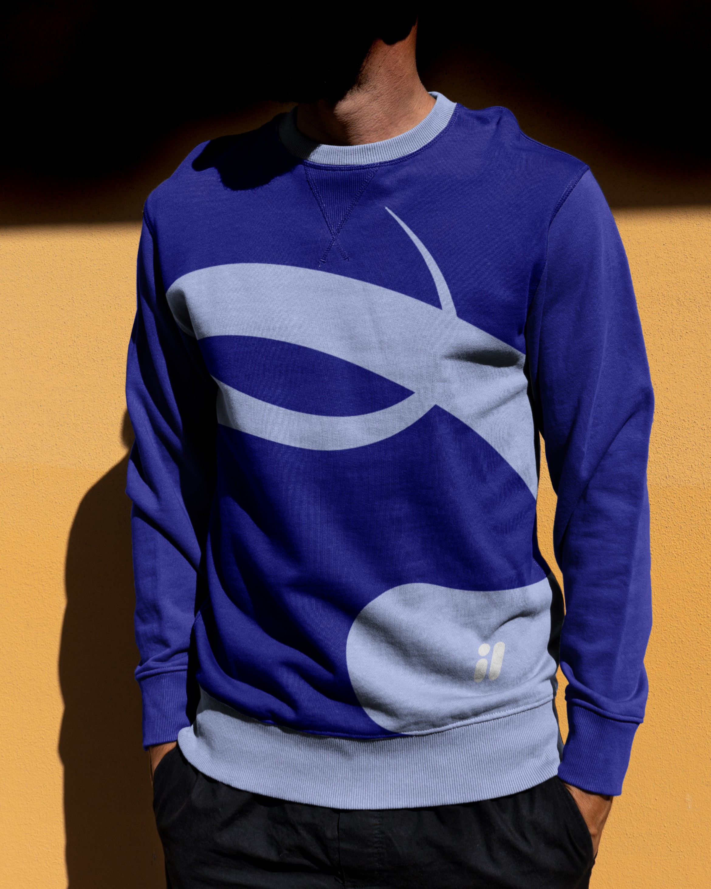 Blue sweatshirt printed with an oversized pale swoosh graphic and 'il' mark, on an ochre wall