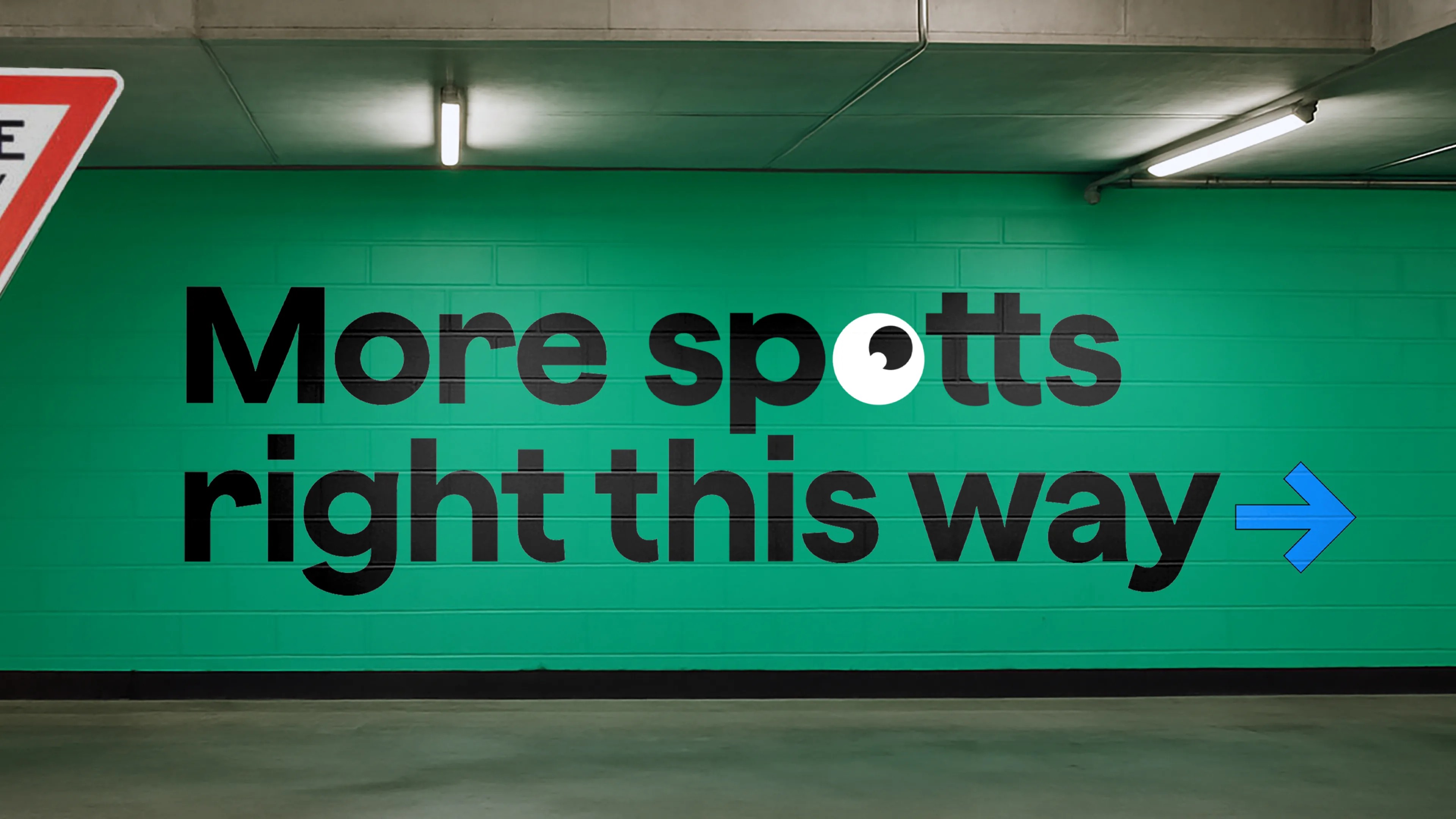 Car park wall painted green with 'More spotts right this way' wayfinding type and a blue arrow