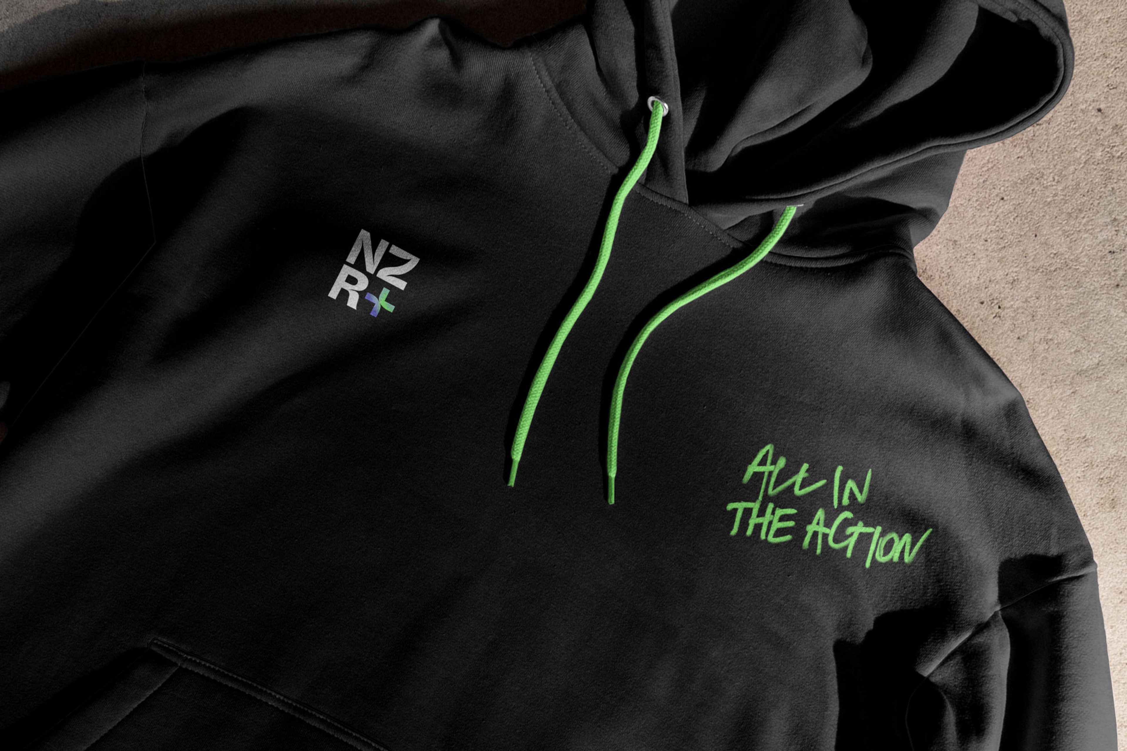 Black hoodie with an embroidered NZR+ mark, neon green drawcords and 'All in the action' script
