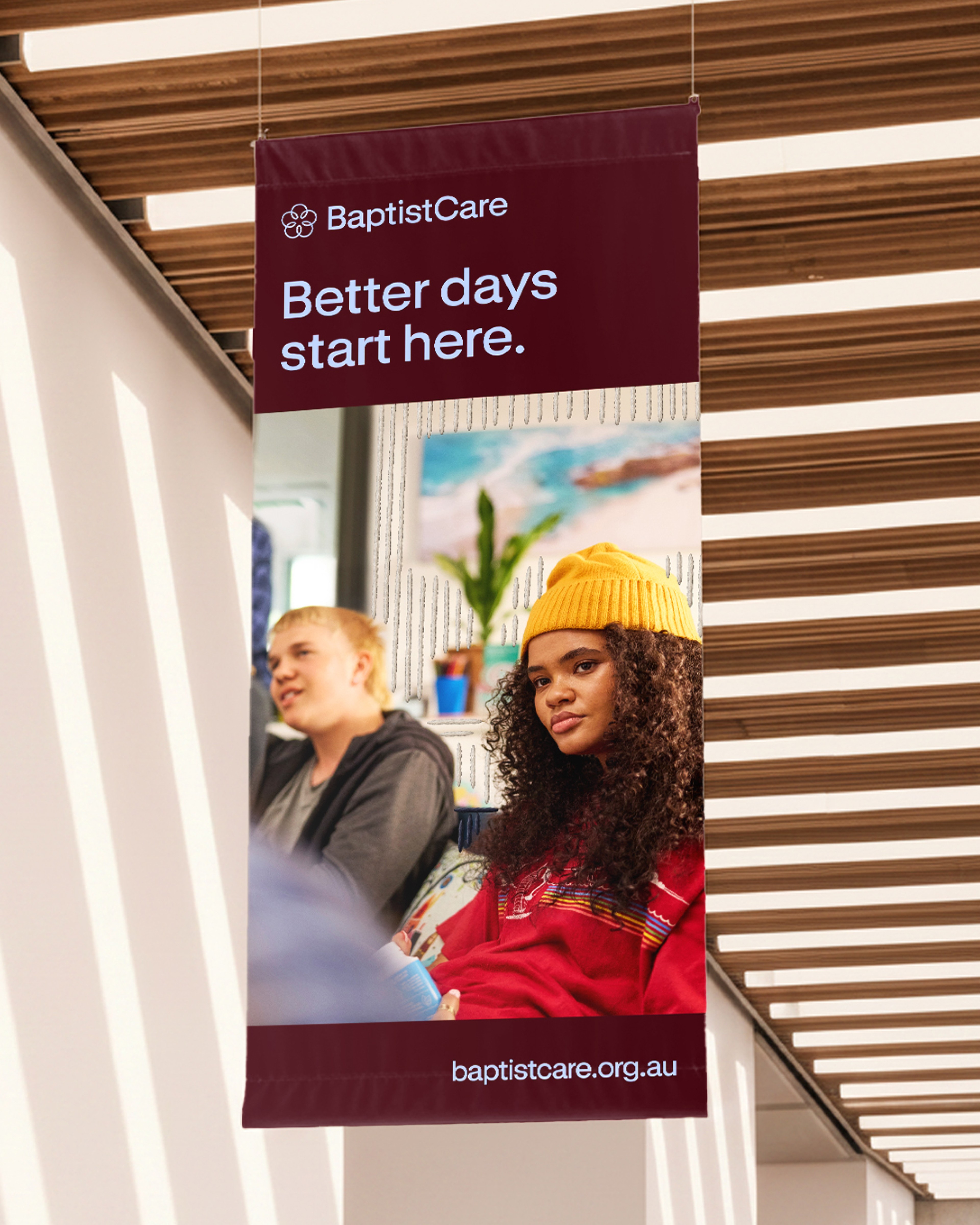 Maroon hanging banner reading "Better days start here." in a sunlit, slatted-ceiling foyer