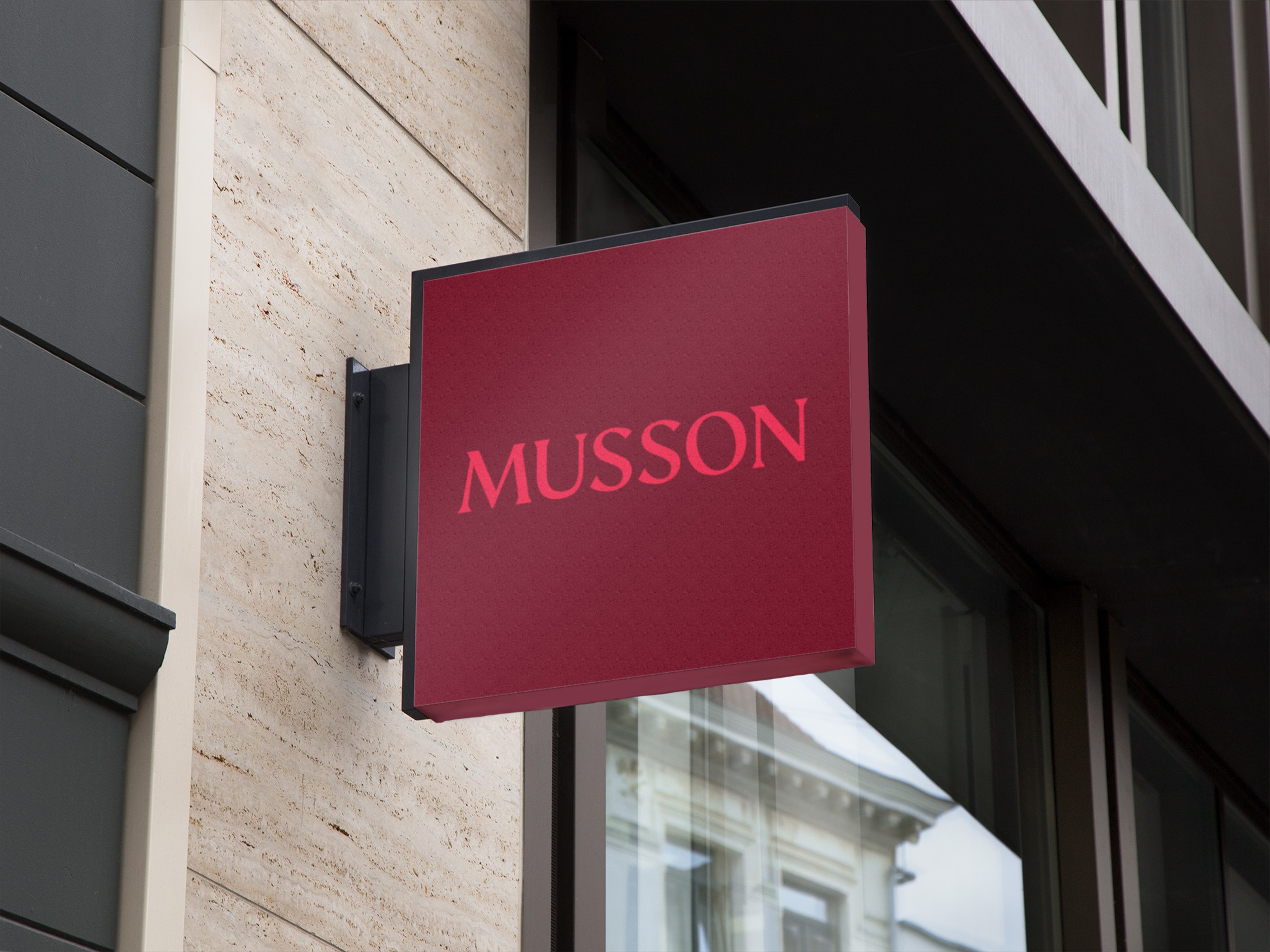 Projecting blade sign in deep red carrying the Musson wordmark on a stone building facade