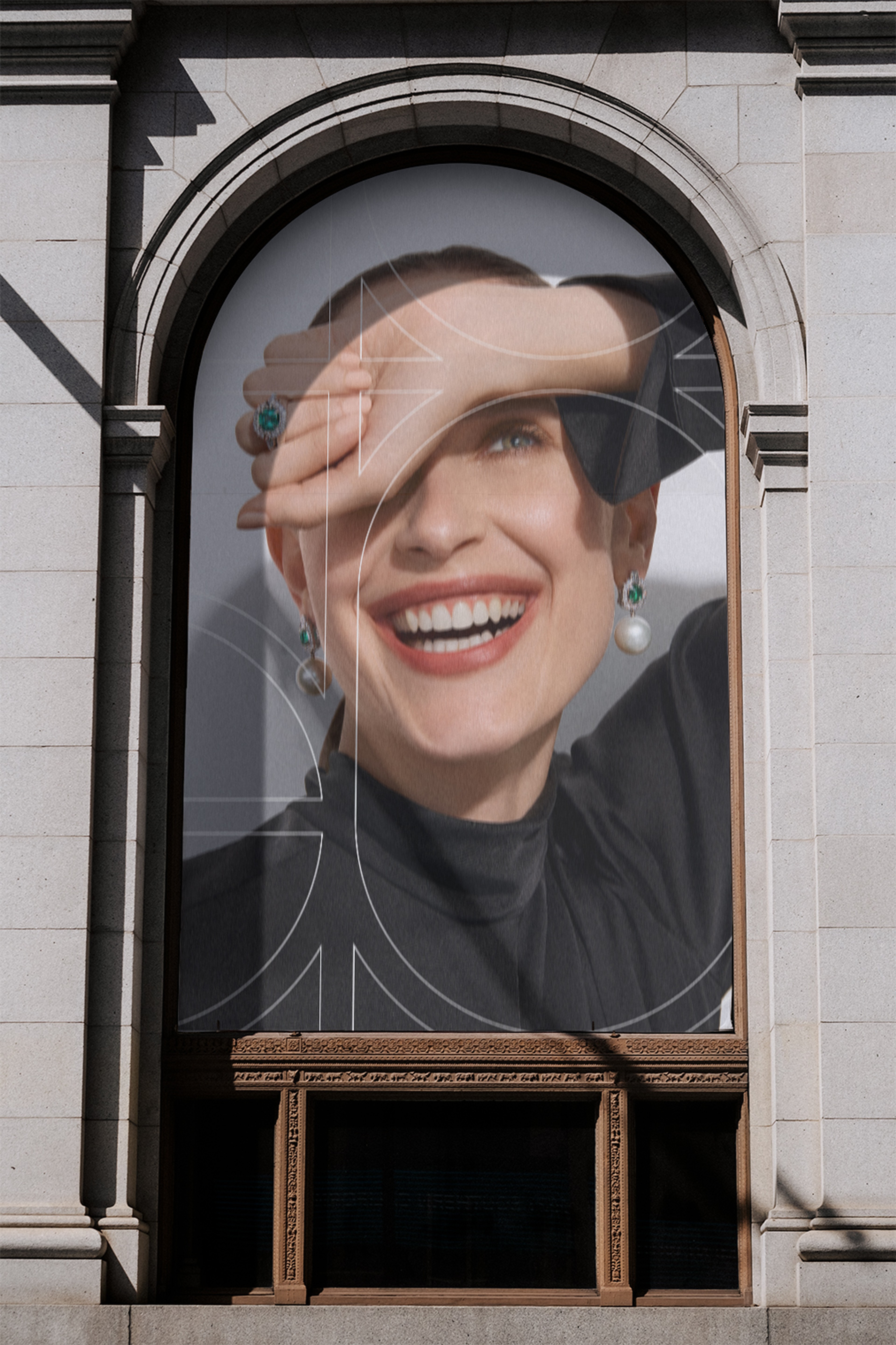 Arched window poster of a smiling model in emerald and pearl jewellery, overlaid with monogram lines