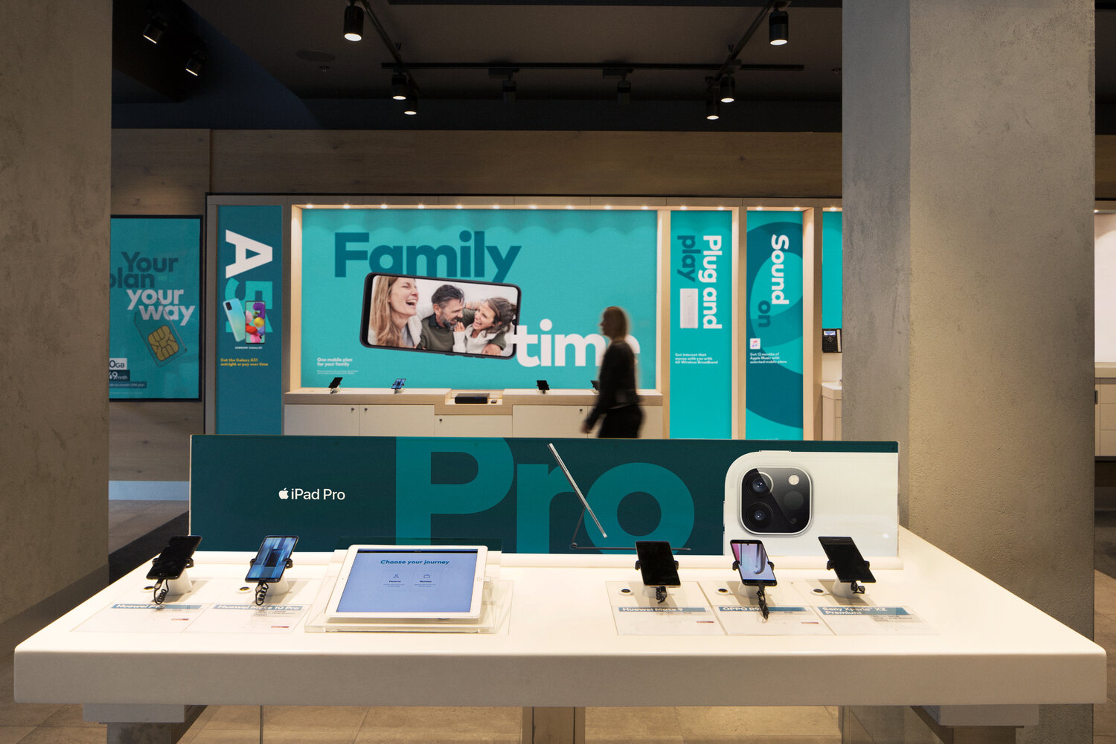 Optus retail interior with teal in-store signage and a device display table for iPad Pro
