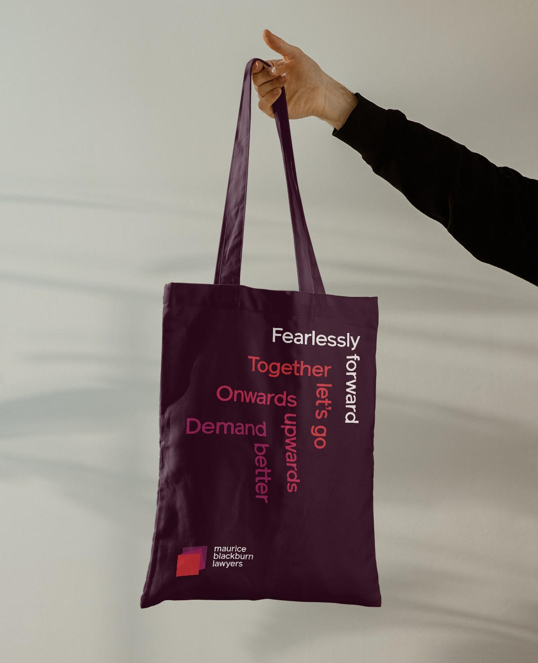 Plum tote bag printed with interlocking brand lines including 'Fearlessly forward' and 'Demand better'