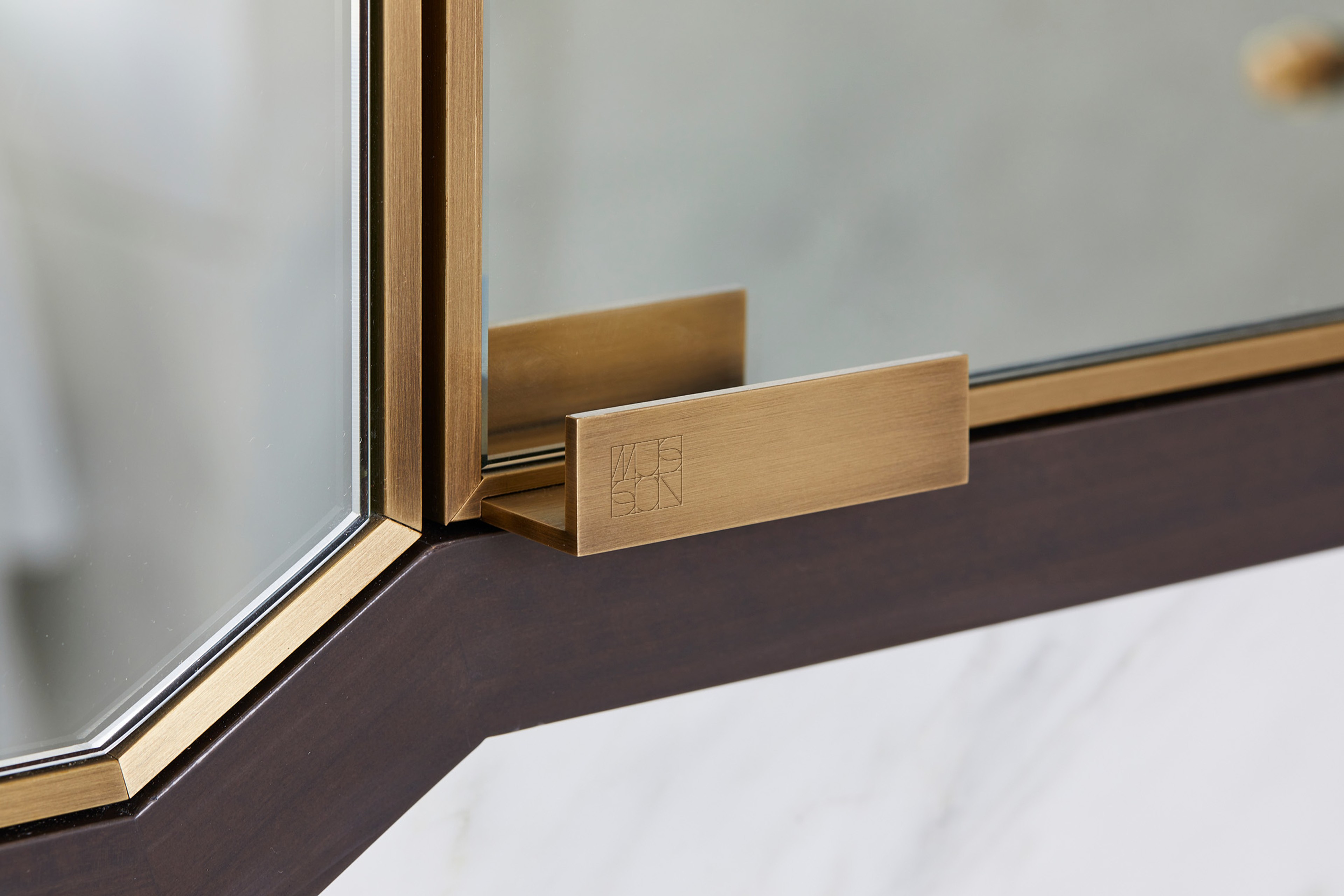 Brushed brass display-case handle engraved with the Musson monogram, shot in close-up