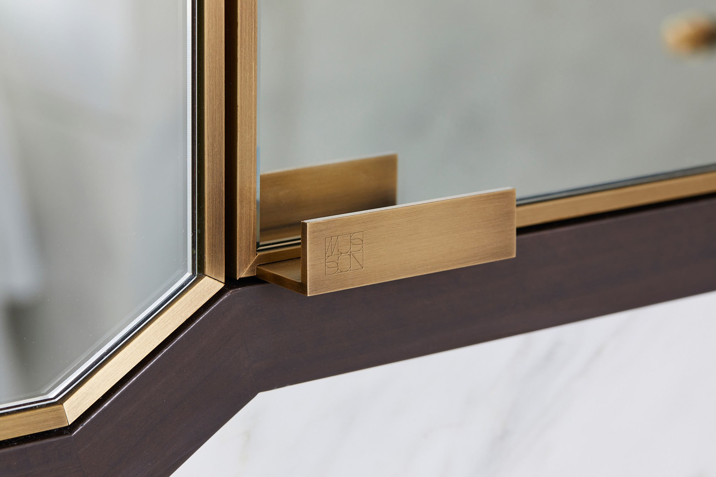 Brushed brass display-case handle engraved with the Musson monogram, shot in close-up