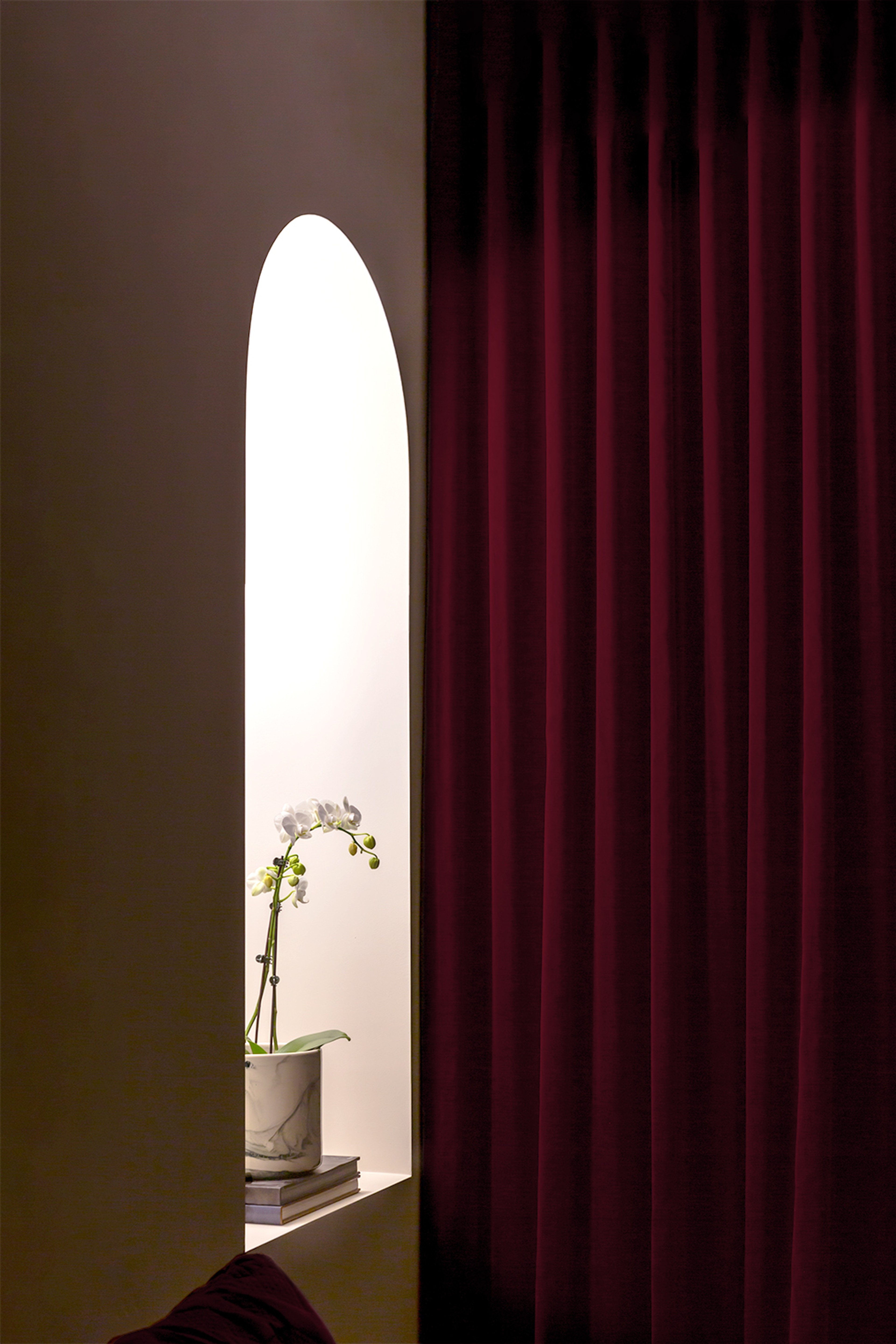 Interior detail: arched niche holding an orchid beside a deep burgundy velvet curtain