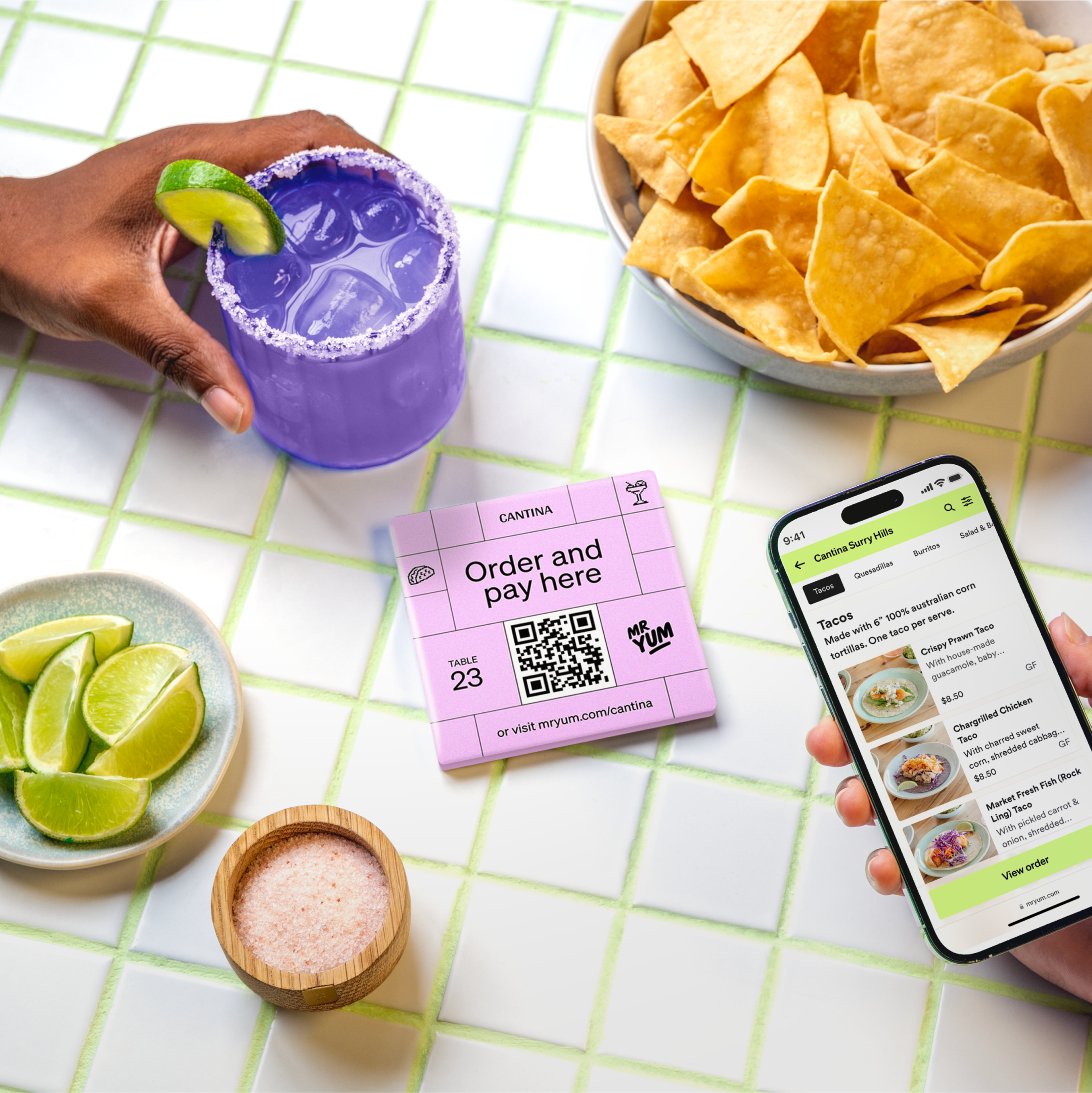 Close crop of the pink QR table card, tortilla chips and a hand holding a purple margarita
