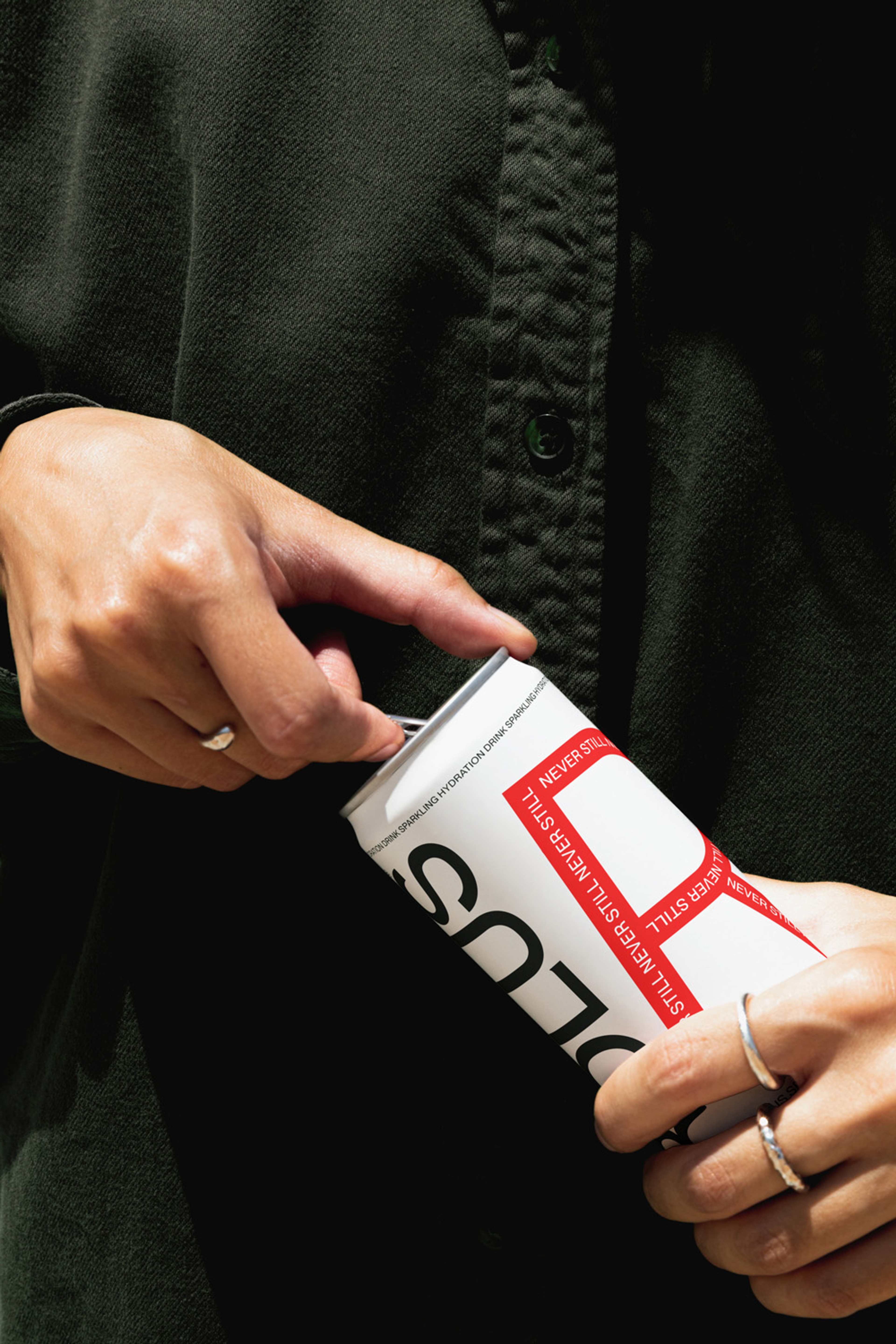 Hands cracking open a white and red can against a black shirt, silver rings catching light