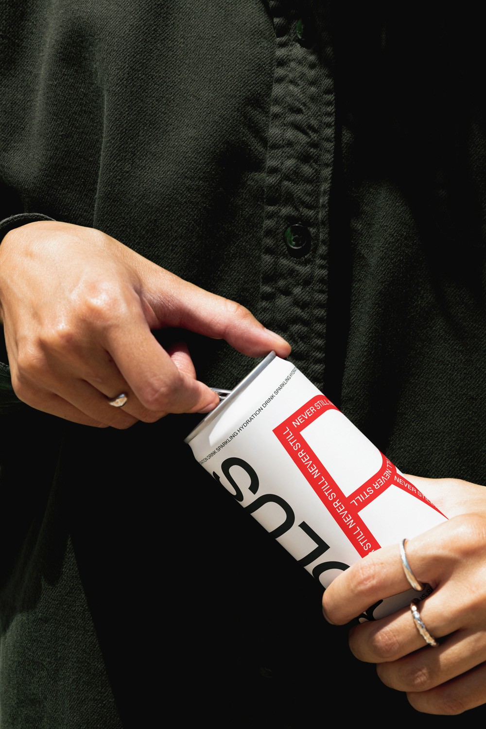 Hands cracking open a white and red can against a black shirt, silver rings catching light