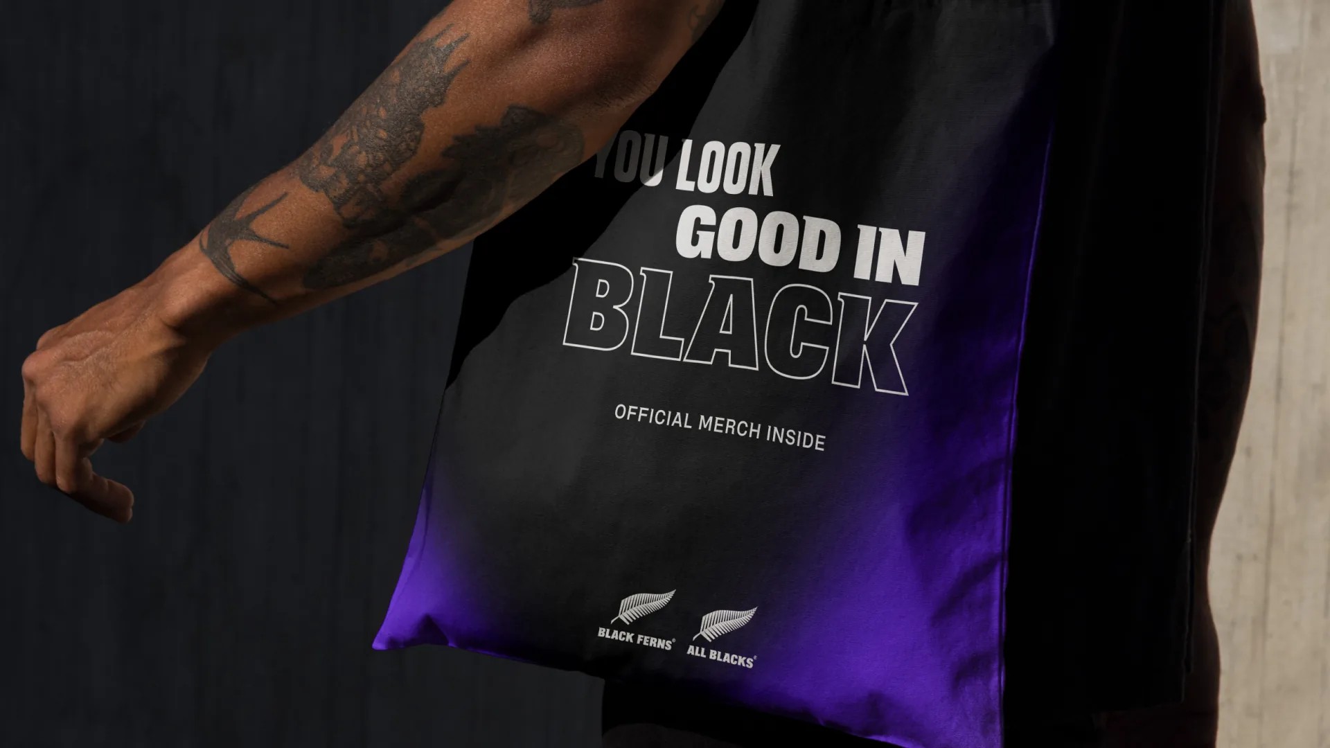 Merch tote in gradient black and purple, both teams' silver fern logos at its base