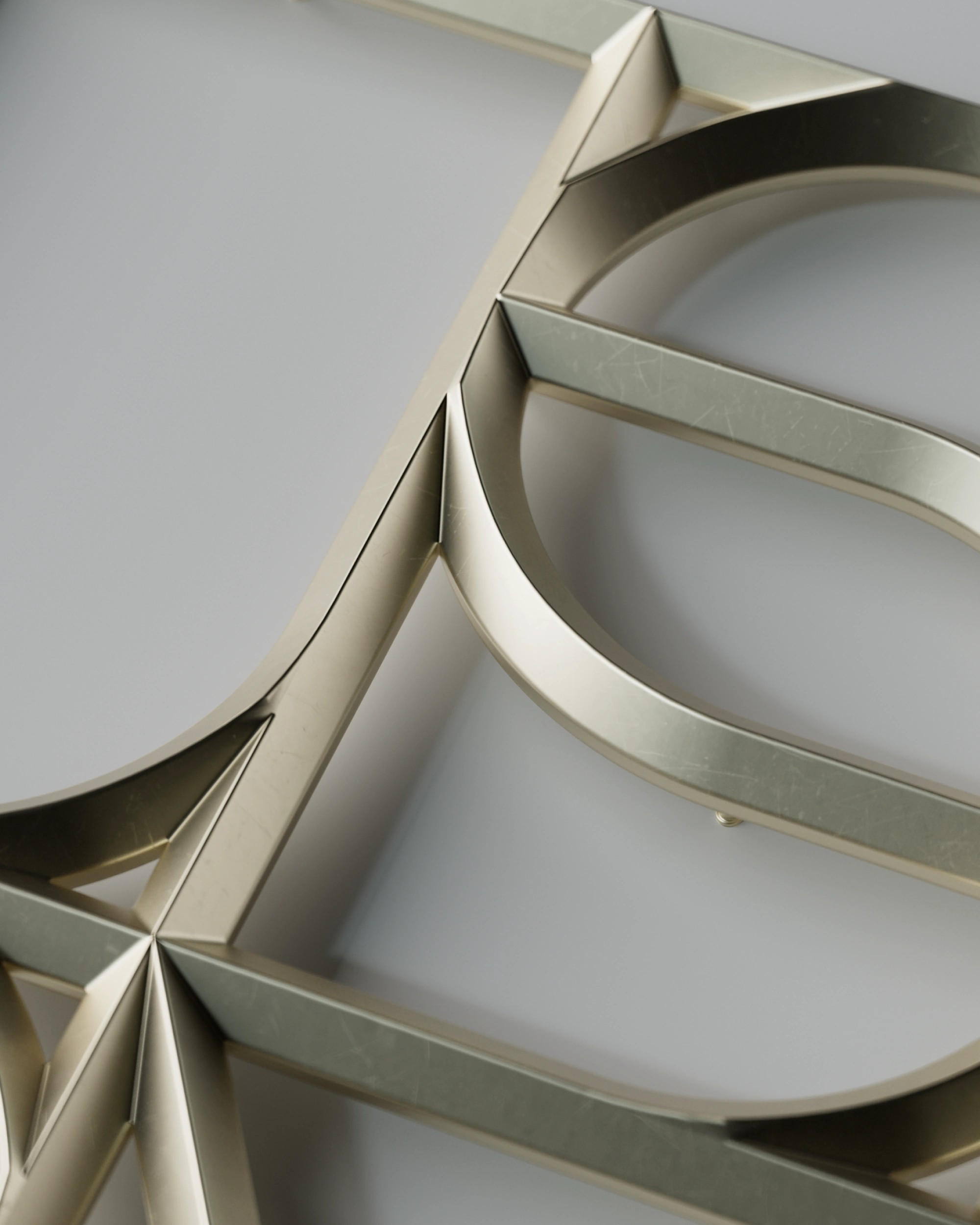 Close-up of a brushed gold monogram sign, geometric cut-out letterforms in raking light