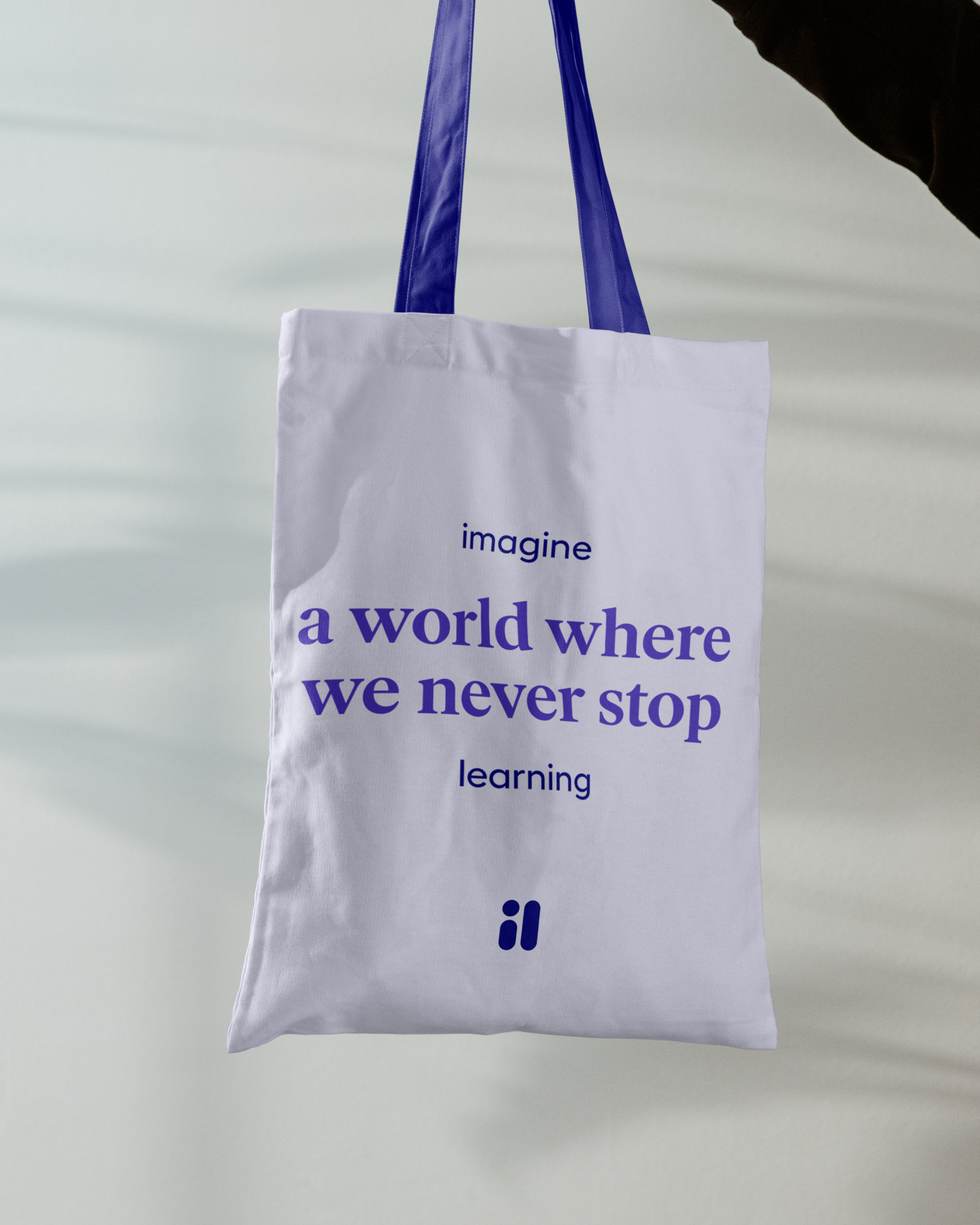 Tote bag printed with the Imagine Learning manifesto line and monogram in violet