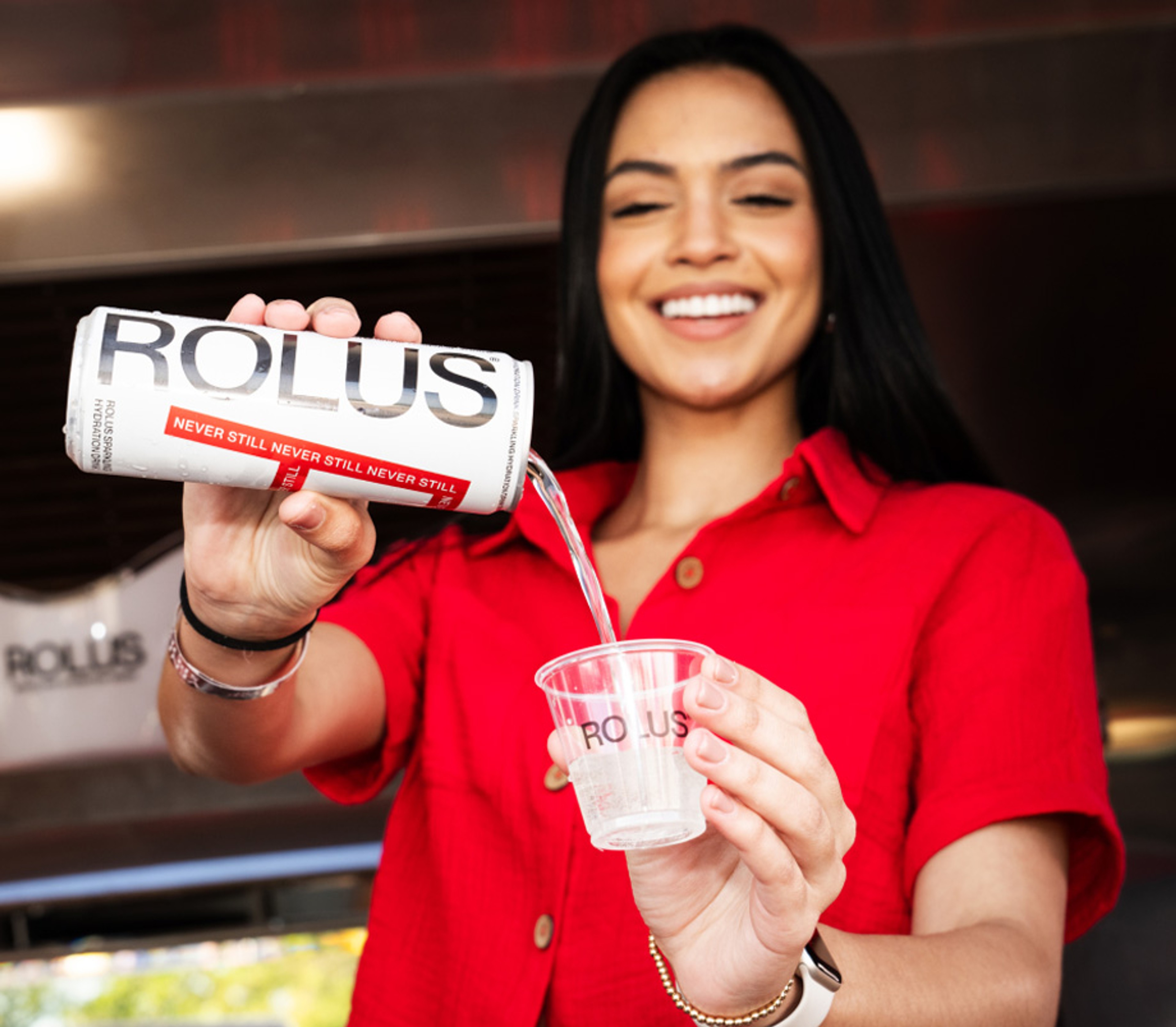 Rolus can poured into a branded cup at a live sampling activation, staff in red shirts