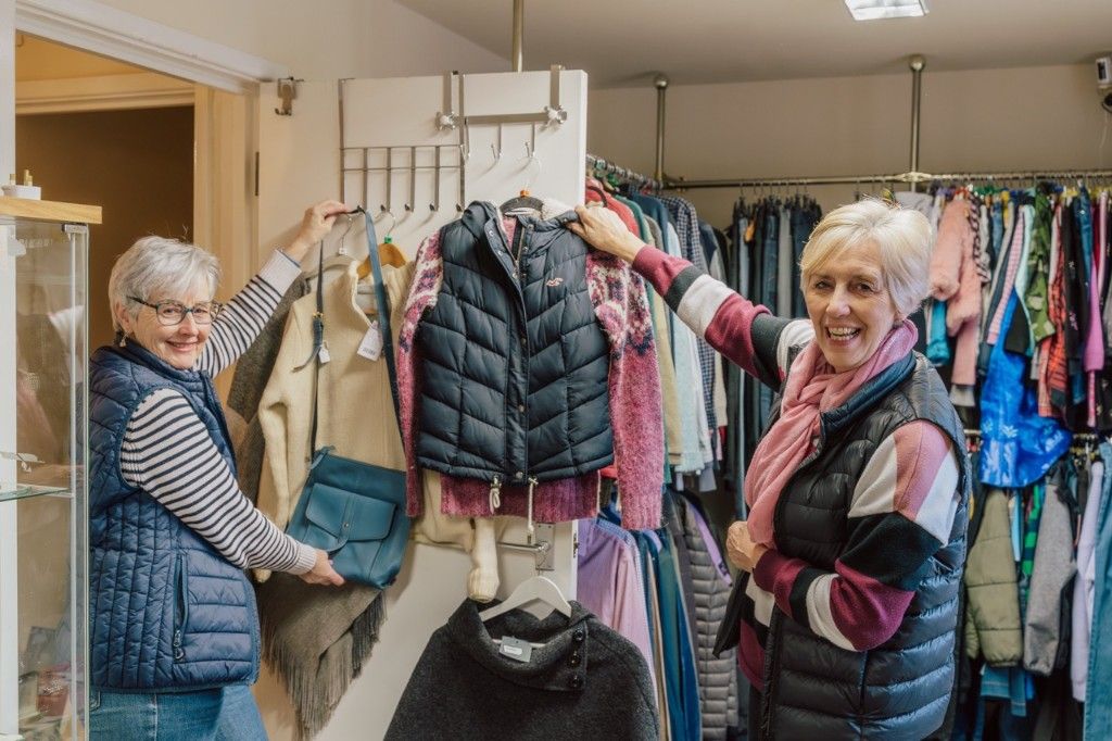 Two volunteers smiling in a Dove Cottage charity shop while arranging clothing