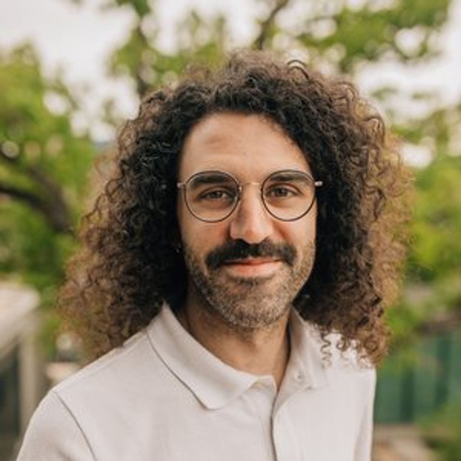 Alex Palmer with curly hair and glasses is smiling for the camera .