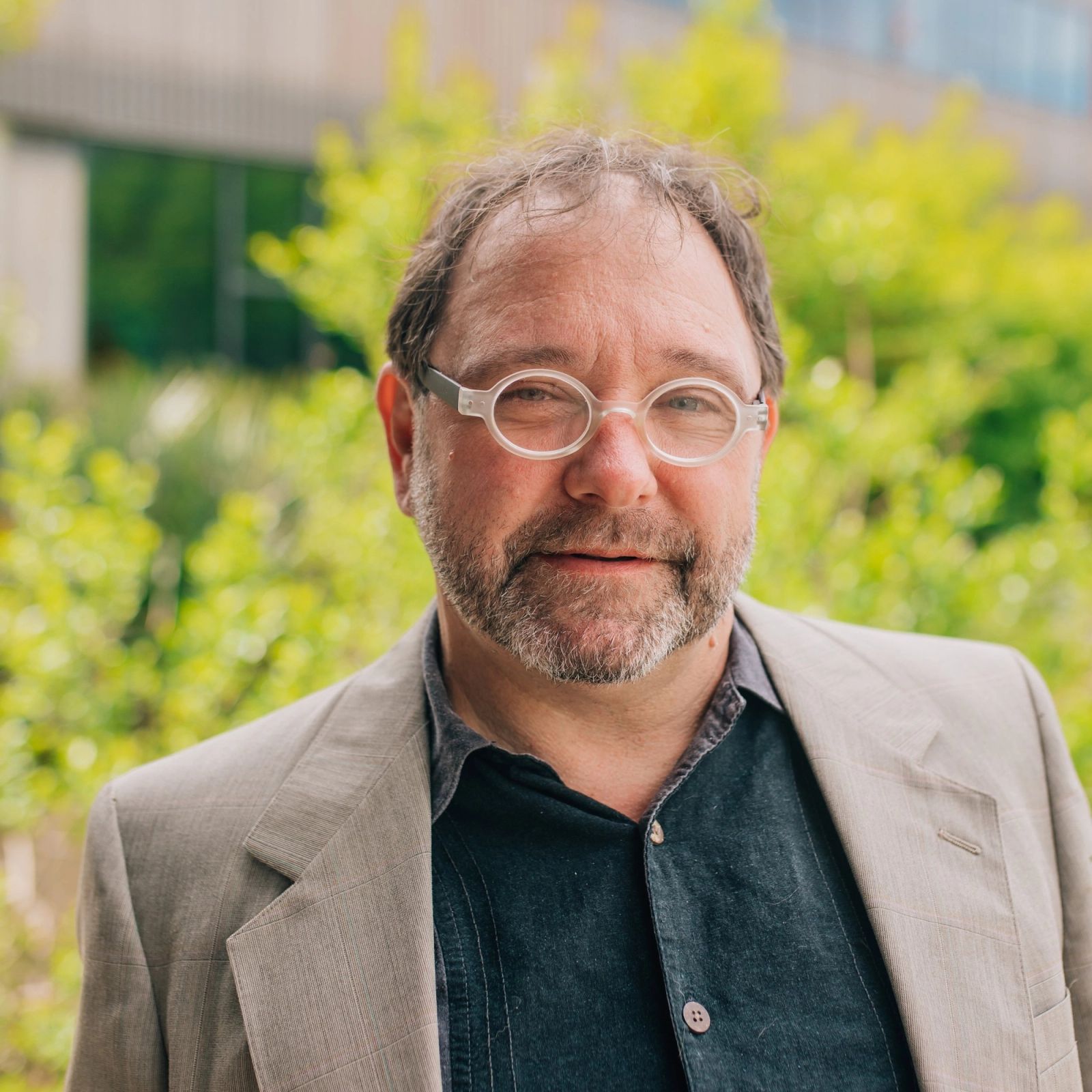 Bryan with a beard and glasses is standing in front of a green background .