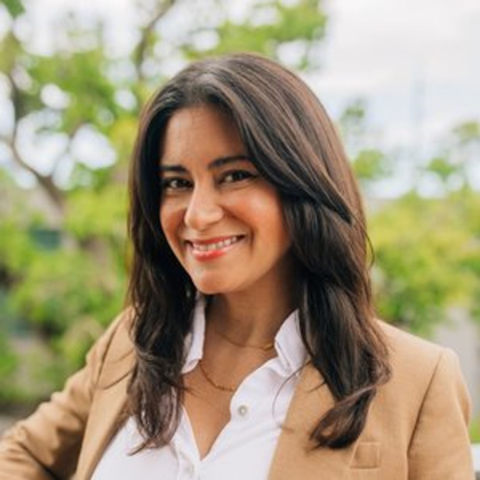 Aixa Solá in a tan jacket and white shirt is smiling for the camera .