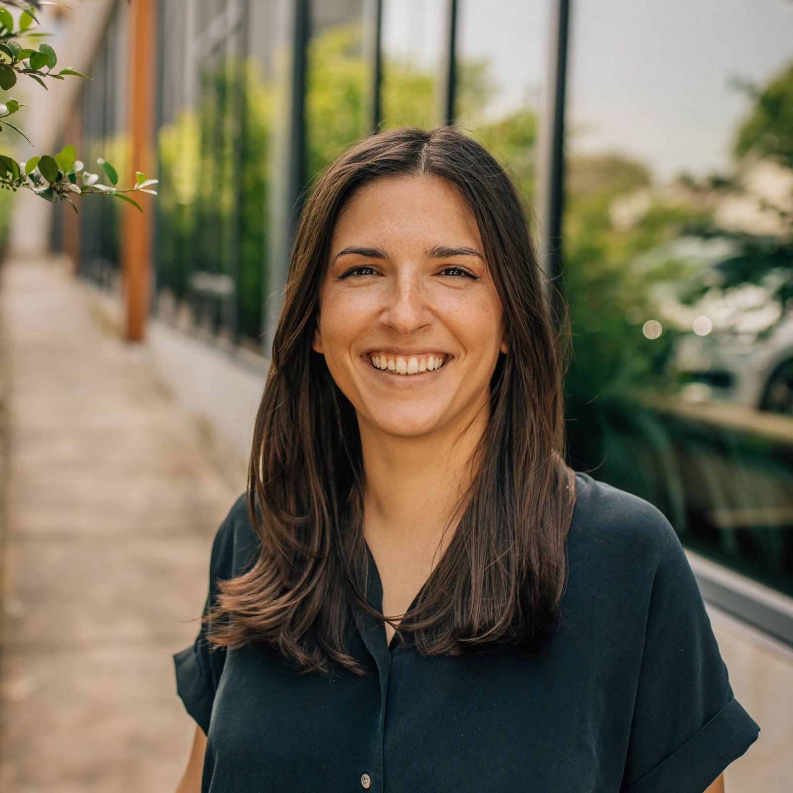 Lindsey is smiling for the camera while standing on a sidewalk in front of a building