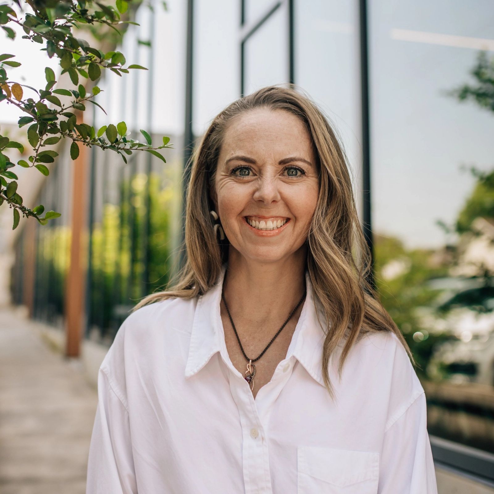 Pam in a white shirt is smiling in front of a building .