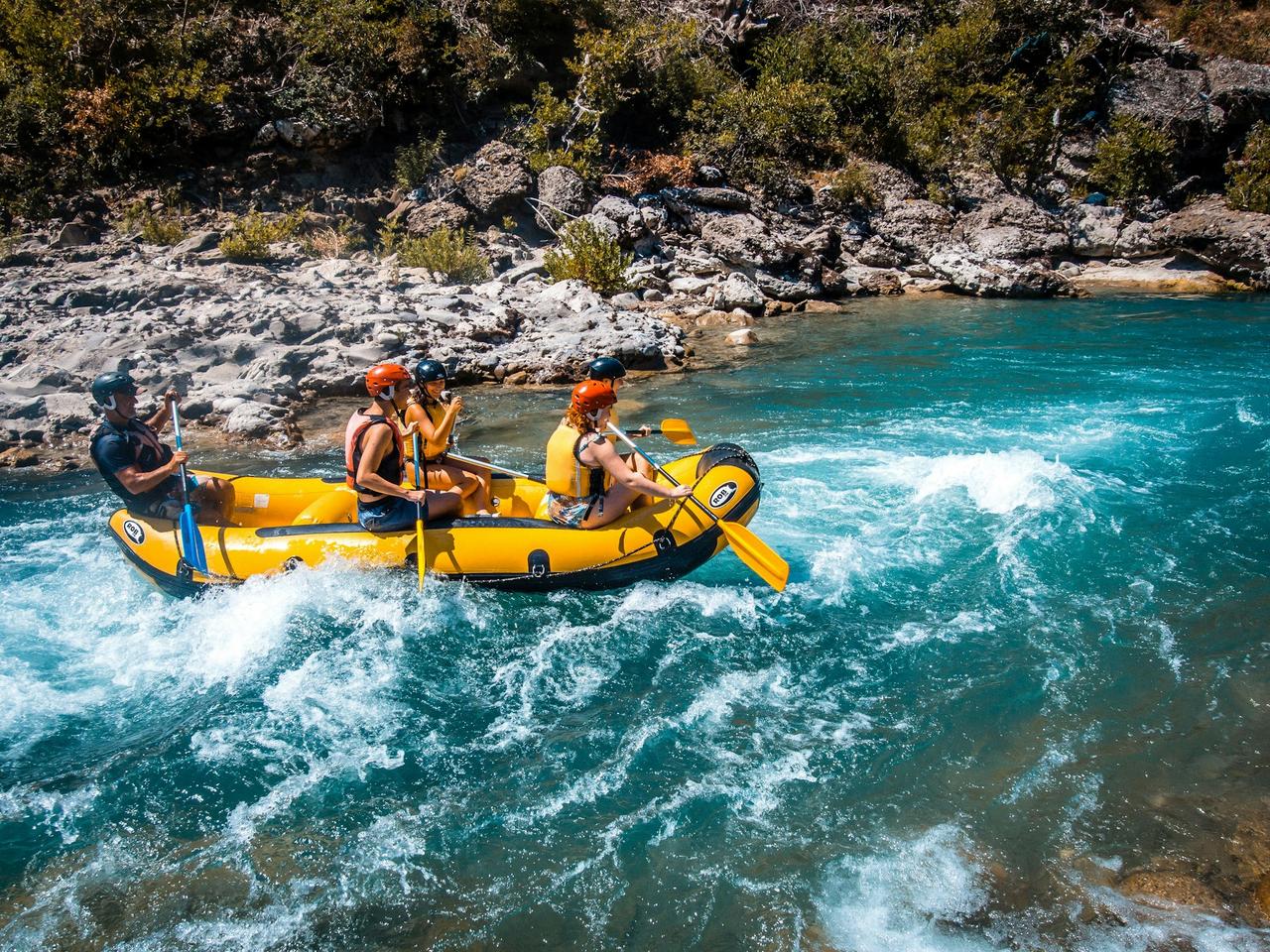 Group in helmets and life jackets paddling a yellow raft through white water