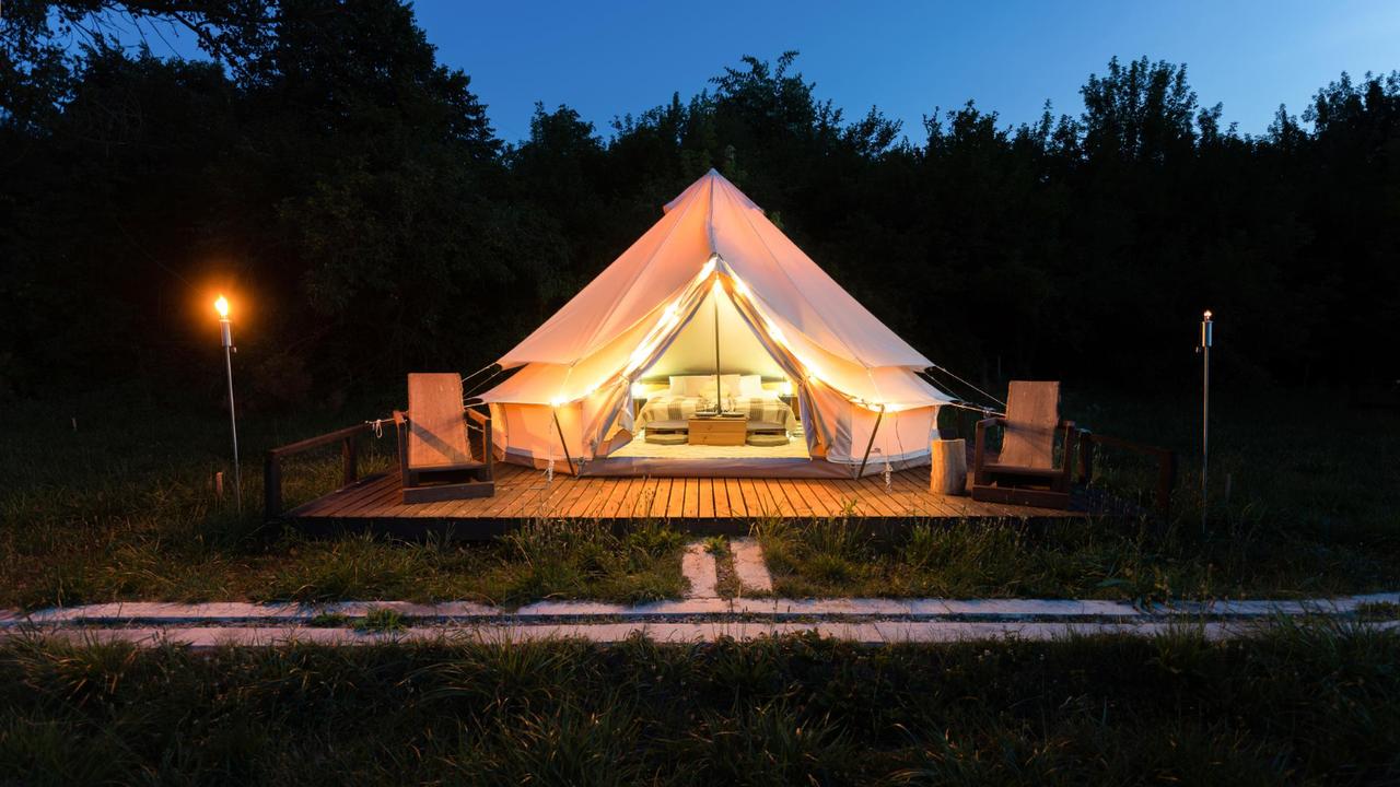 Bell tent on a wooden deck lit up at dusk, with torches on either side