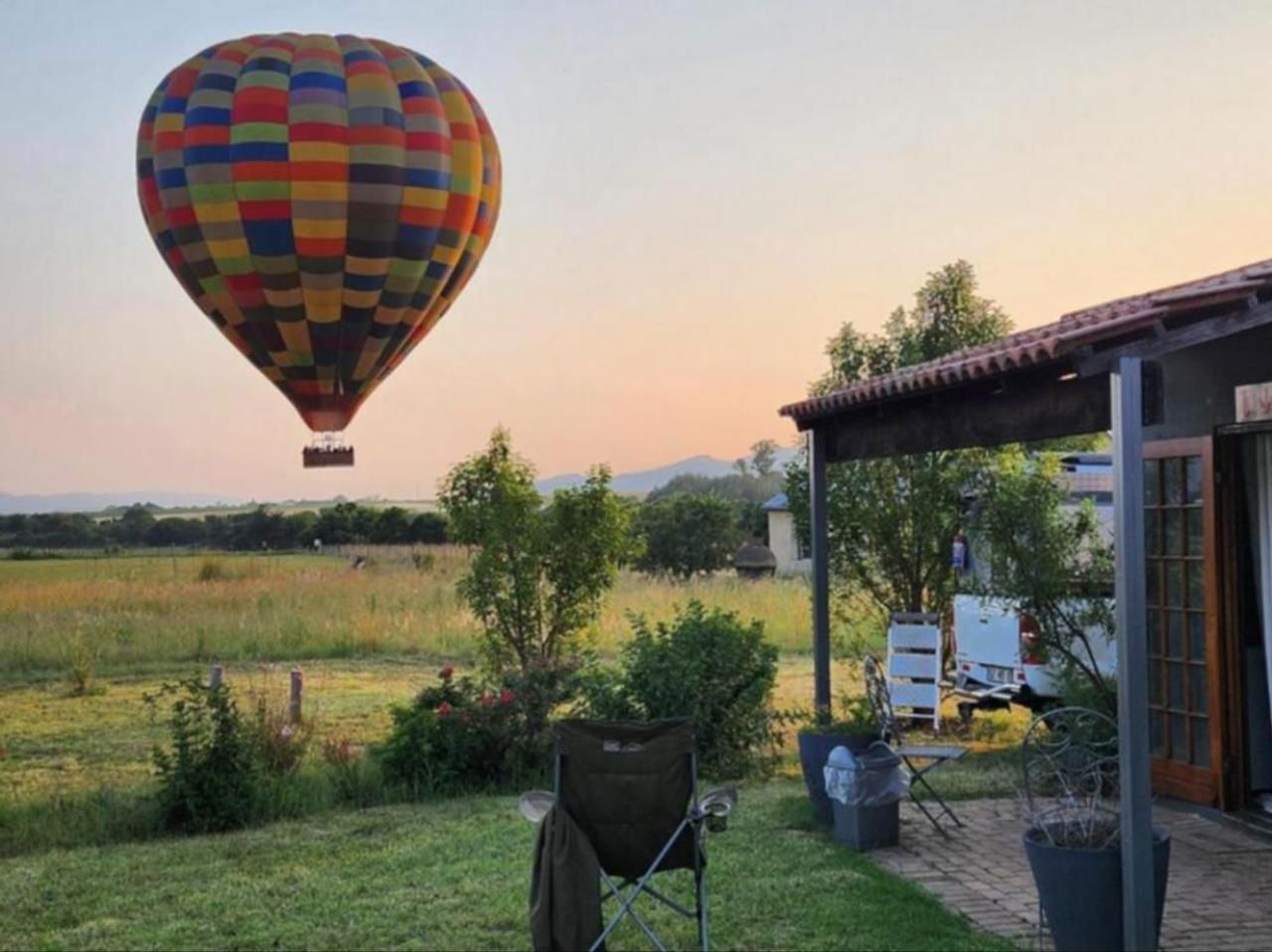A colourful hot air balloon rises at dawn over the garden and cottage patio at Magalies River Country Retreat near Hartbeespoort