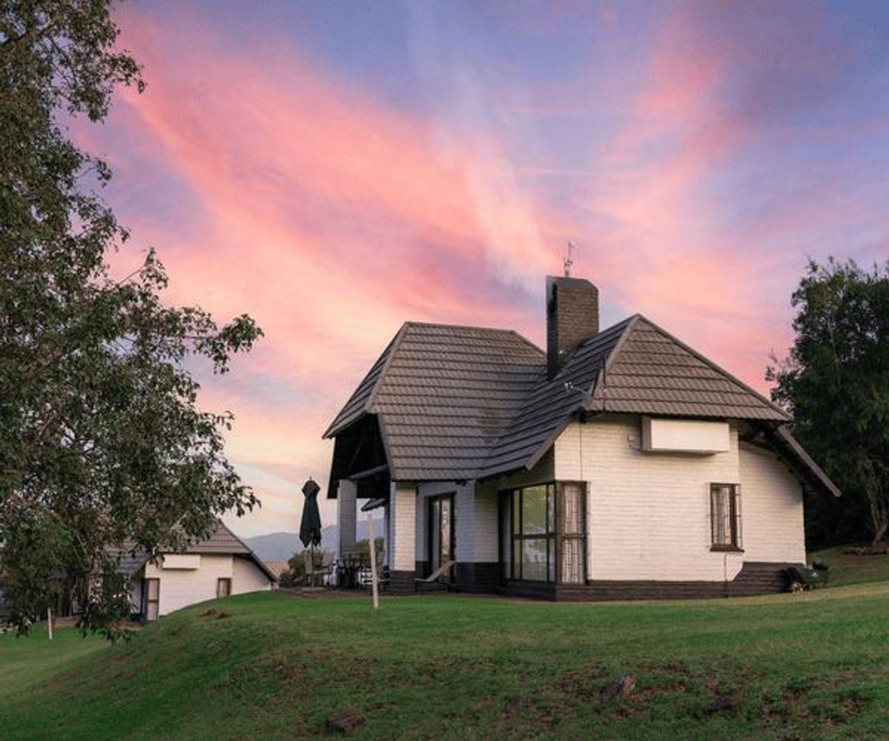 White cottage with a steep tiled roof under a pink sunset sky at Mount Sheba, above Pilgrim’s Rest