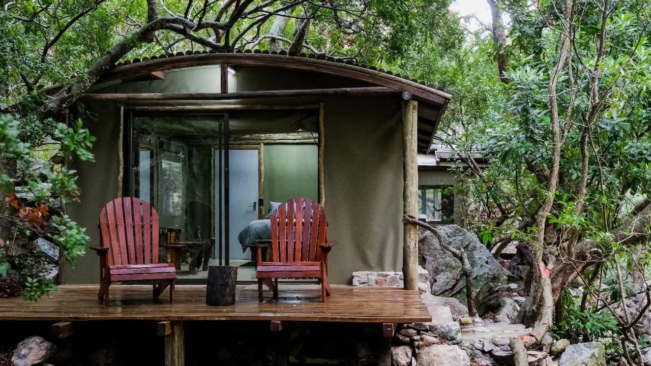 Canvas tent with a curved roof and two red deck chairs, among trees and rocks at Kleinrivier Mountain Escapes