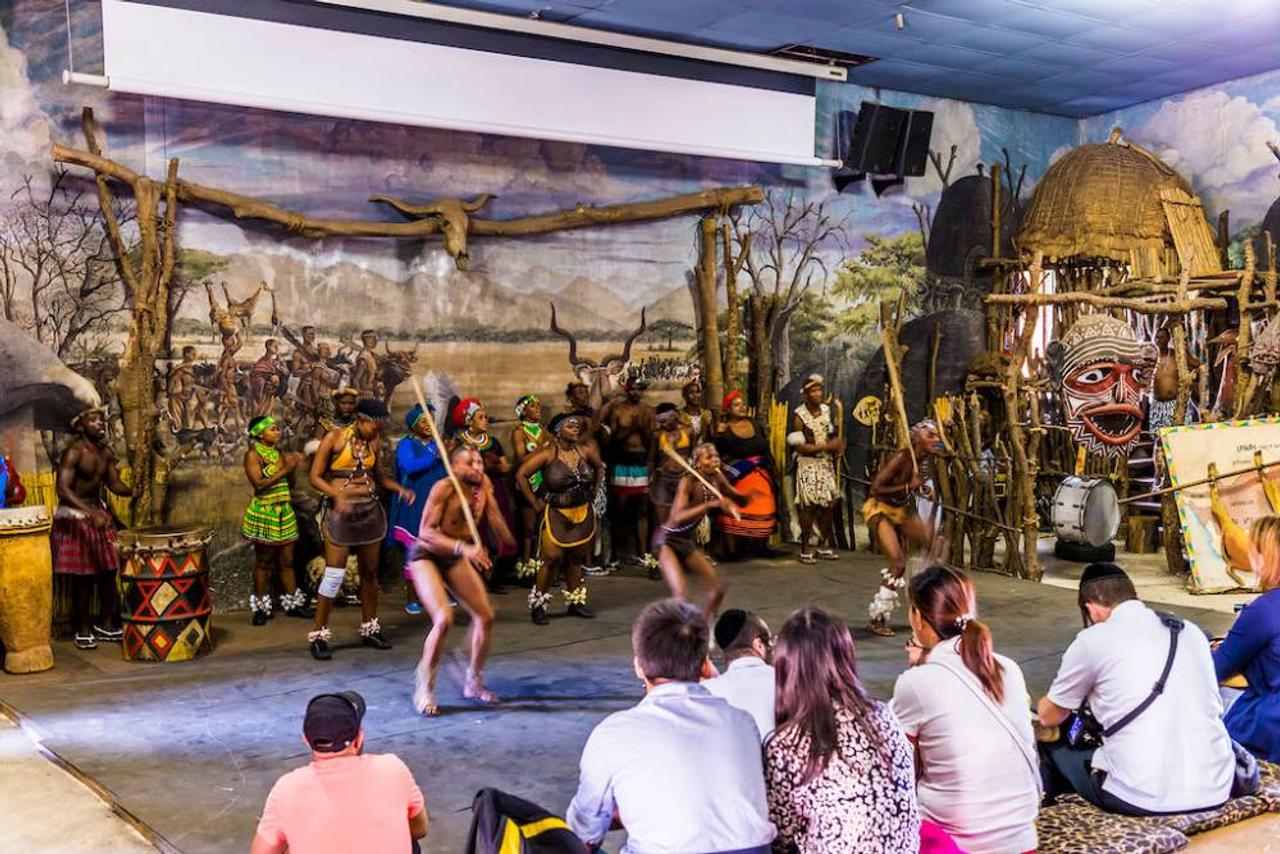 Dancers perform traditional dances for a seated audience in the performance hall at Lesedi Cultural Village